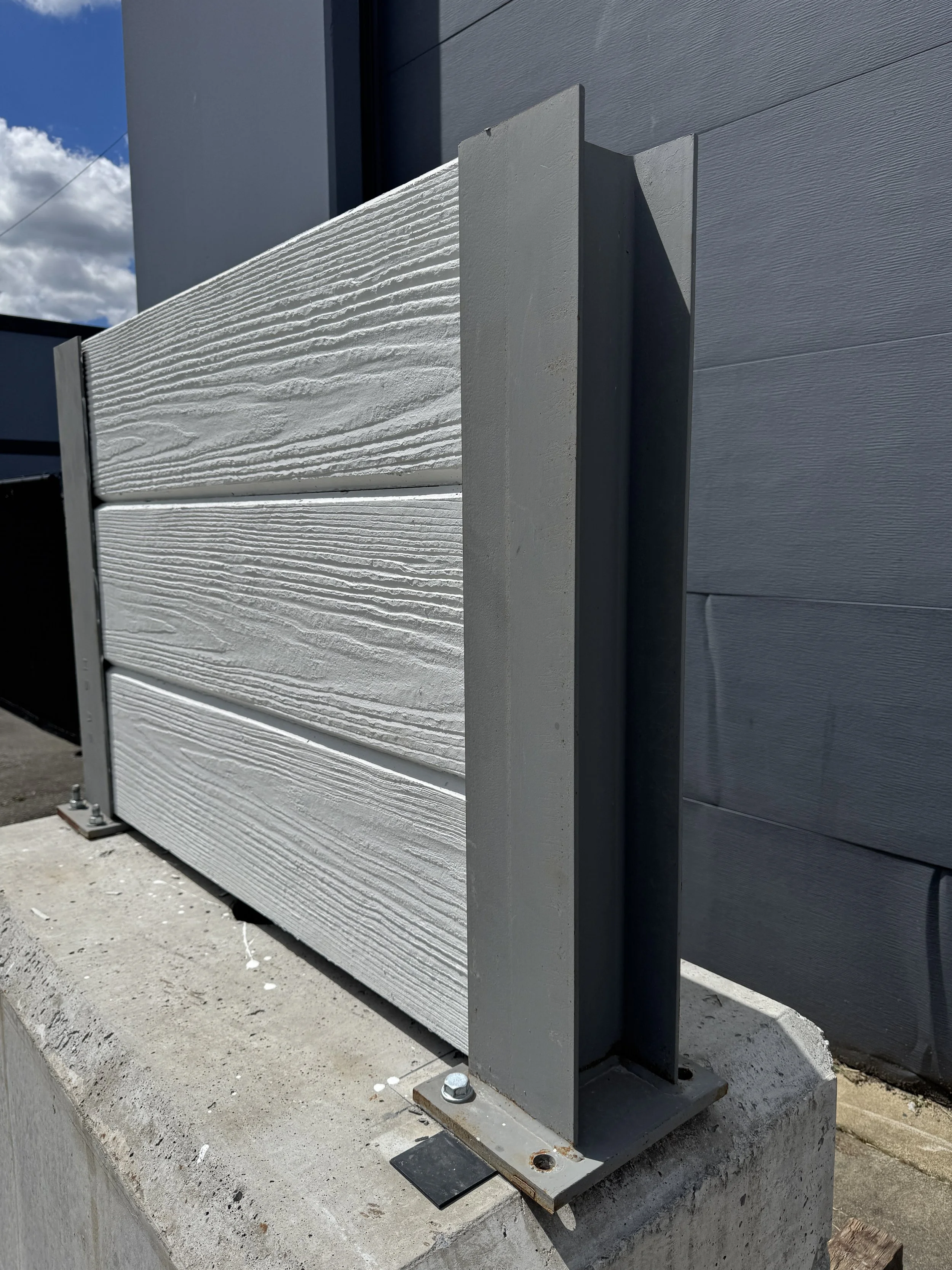 A side-angle photo of a precast fence panel sitting atop a precast concrete block.