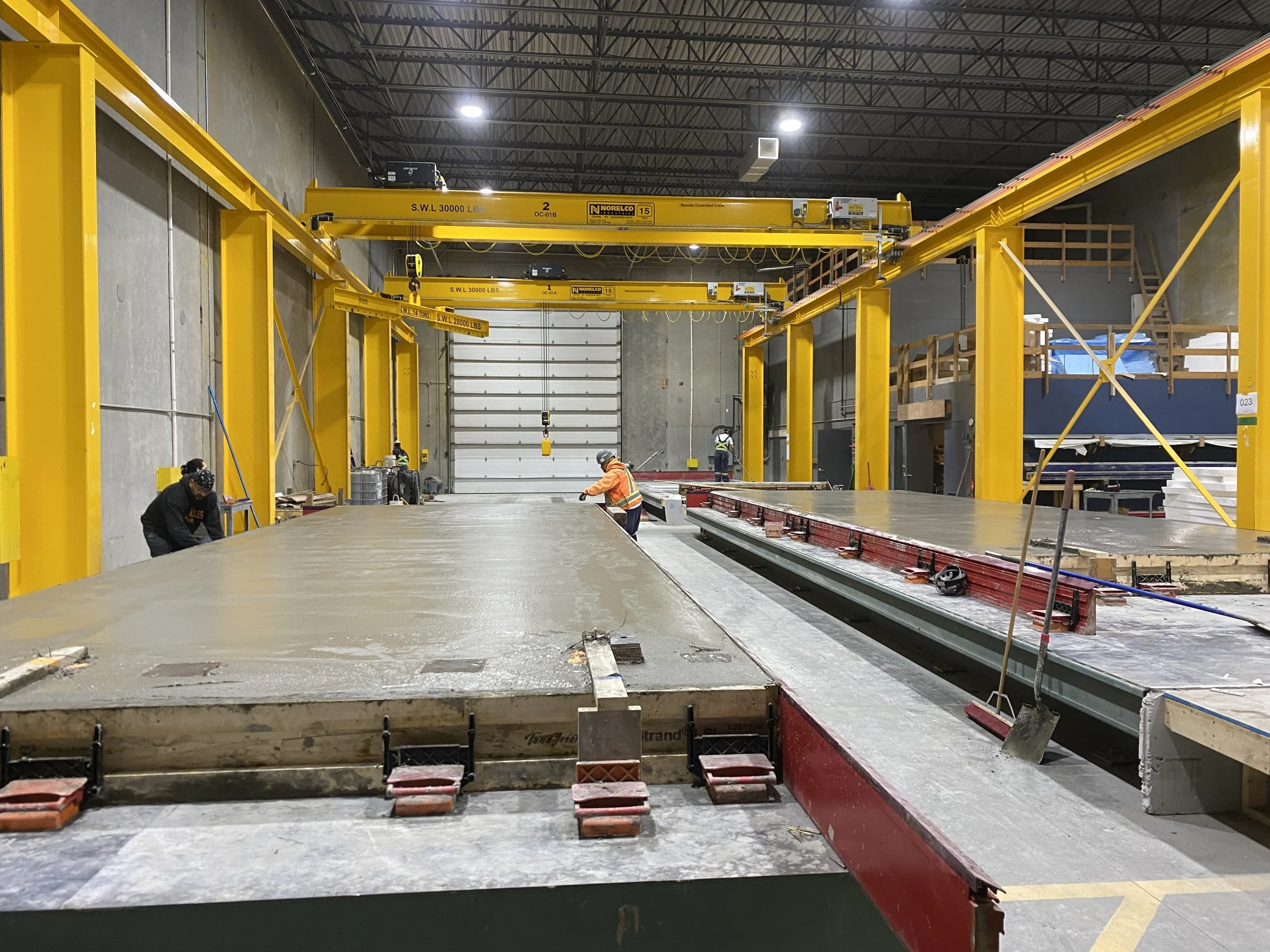 Recently poured precast concrete panels inside an industrial warehouse in Langley, BC, with yellow overhead cranes and large concrete slabs.