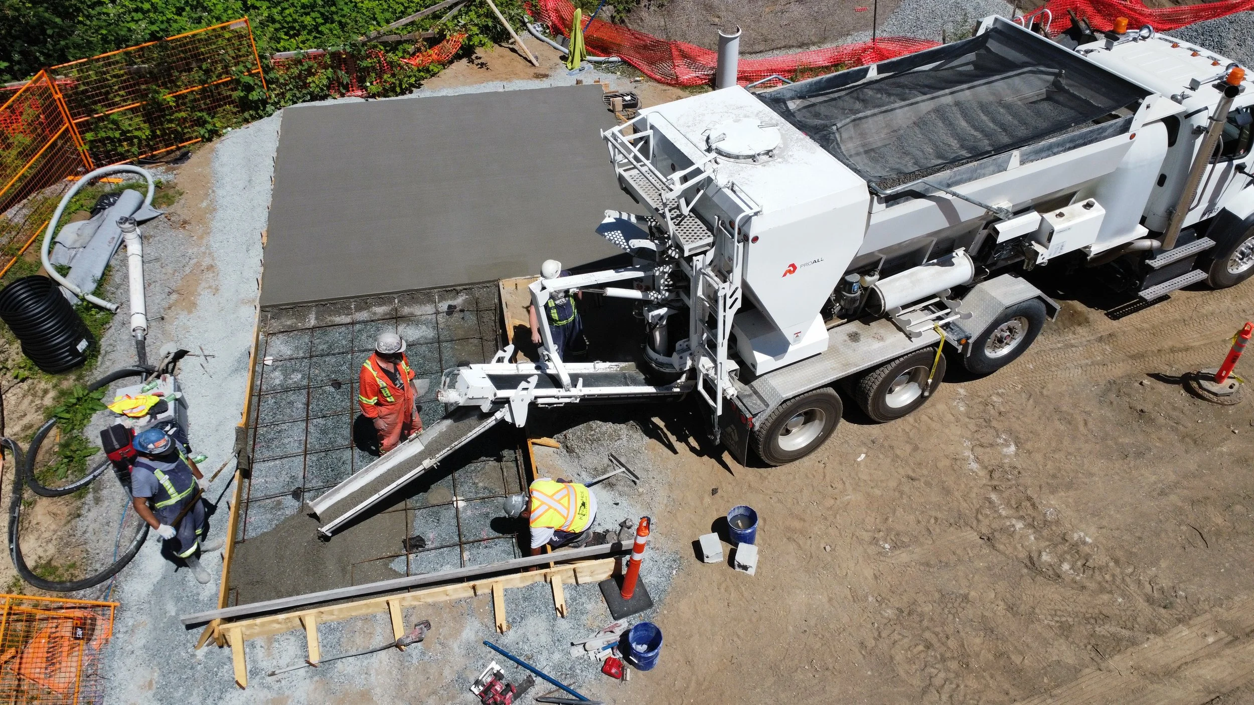 Construction workers pouring concrete on a building site with a large cement mixer truck and orange safety barriers.