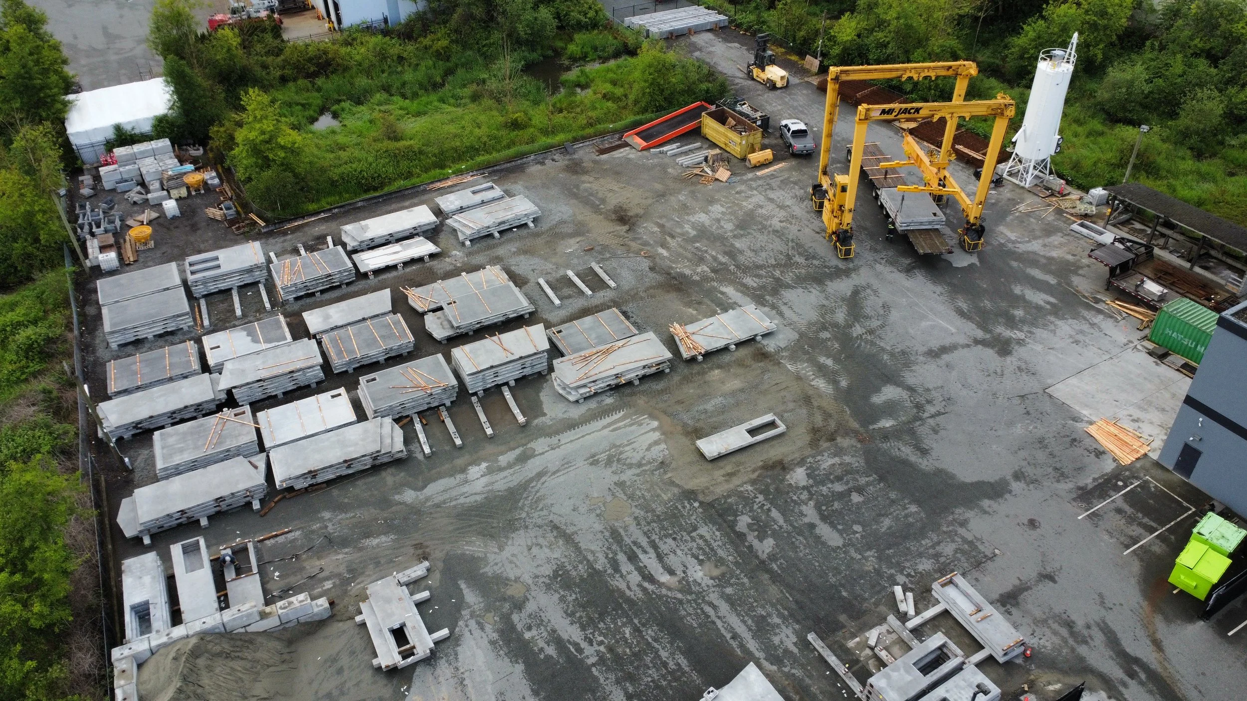 Aerial view of the Baseline Concrete precast yard located in Langley, BC, with stacked concrete slabs, construction equipment, and vehicles surrounded by trees.