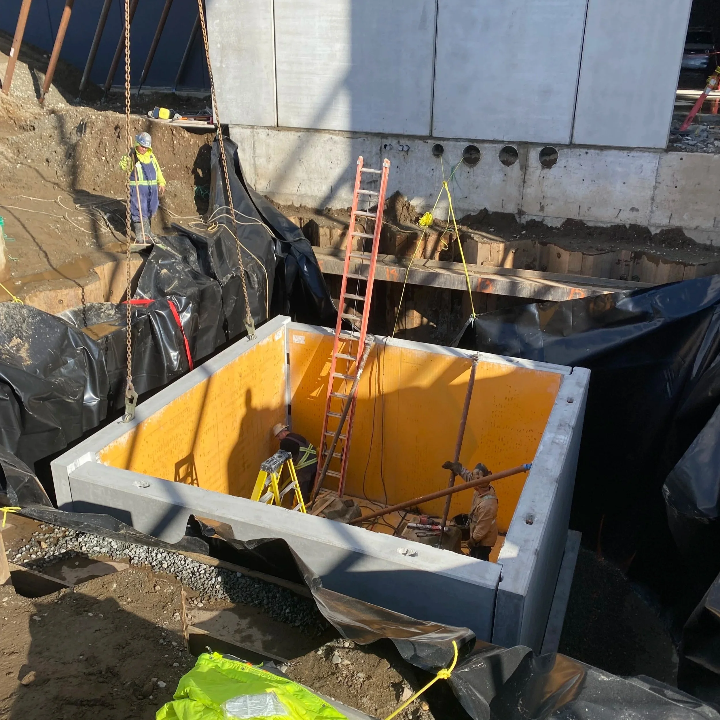 Precast Concrete installation specialists working on a precast water chamber with a concrete wall, ladders, and safety equipment working on an excavation.
