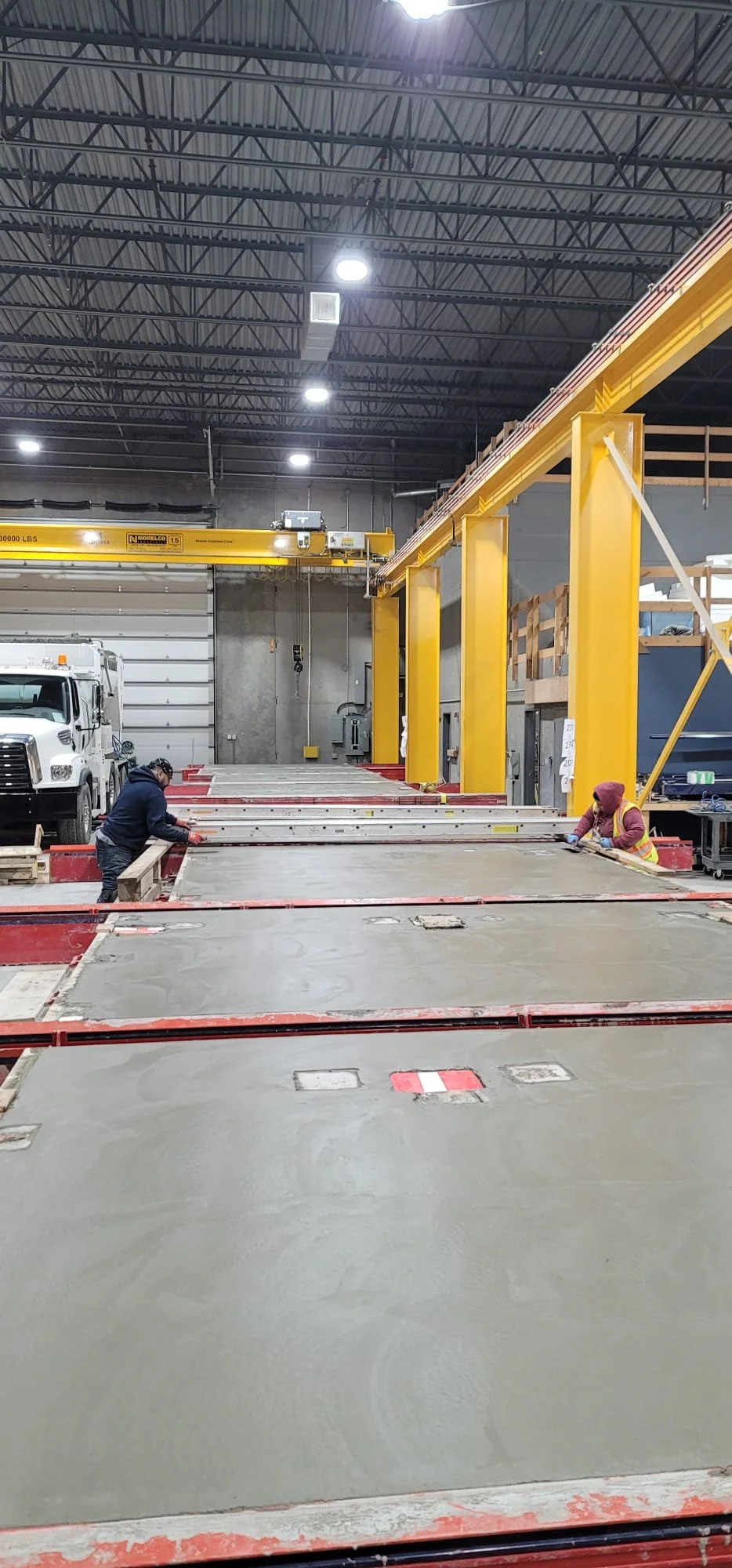 Two workers finishing a precast concrete wall panel, with a number of other panels in the background.