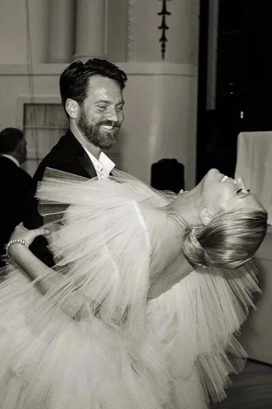 Editorial wedding photographer Melbourne - Aa bride and groom dancing at a wedding reception. The bride is leaning back in the man's arms, smiling, with a large tutu dress and her hair styled in an elegant updo.