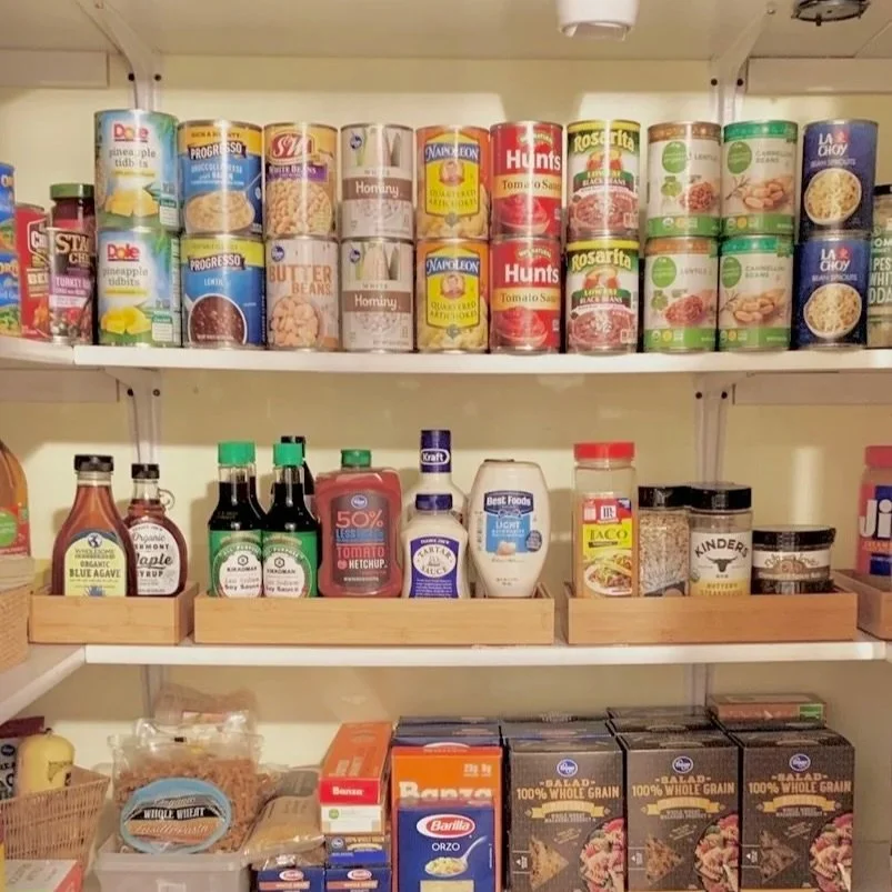 Pantry shelf stocked with canned foods on the top, condiments in the middle, and boxes of grains and pasta on the bottom.