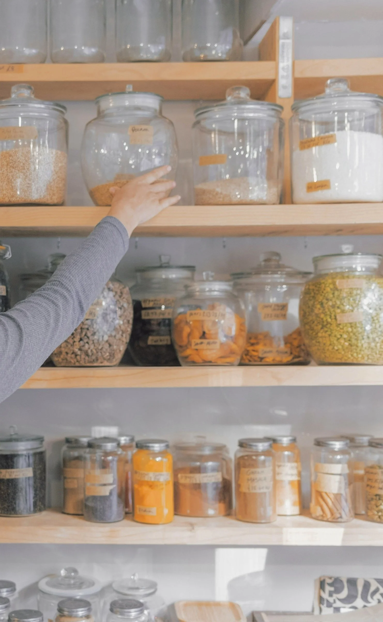 Hand reaching for labeled pantry jar during a professional kitchen organization session.