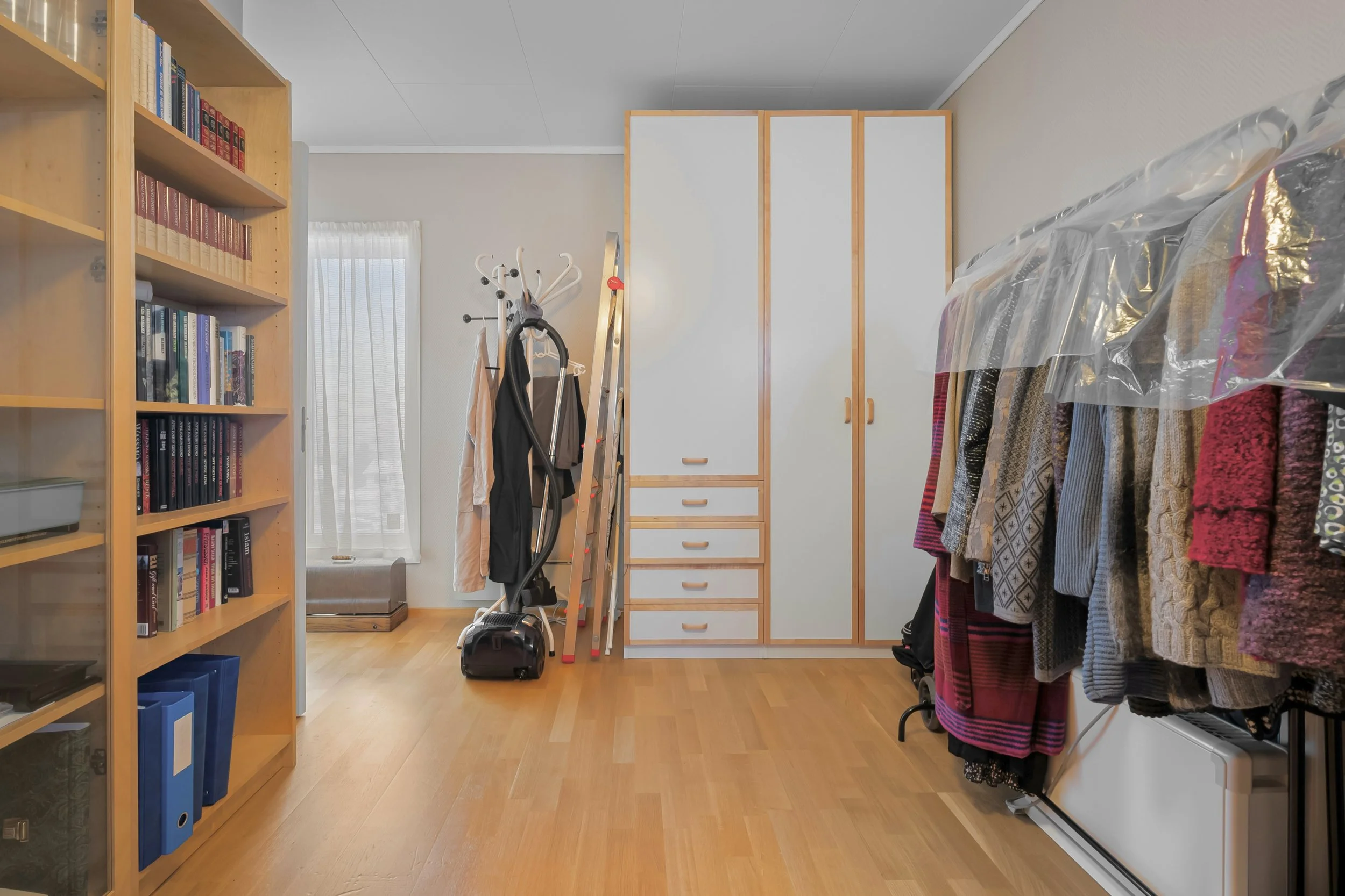 Organized bedroom and closet space with bookshelf, wardrobe, and clothing rack after a home decluttering session.