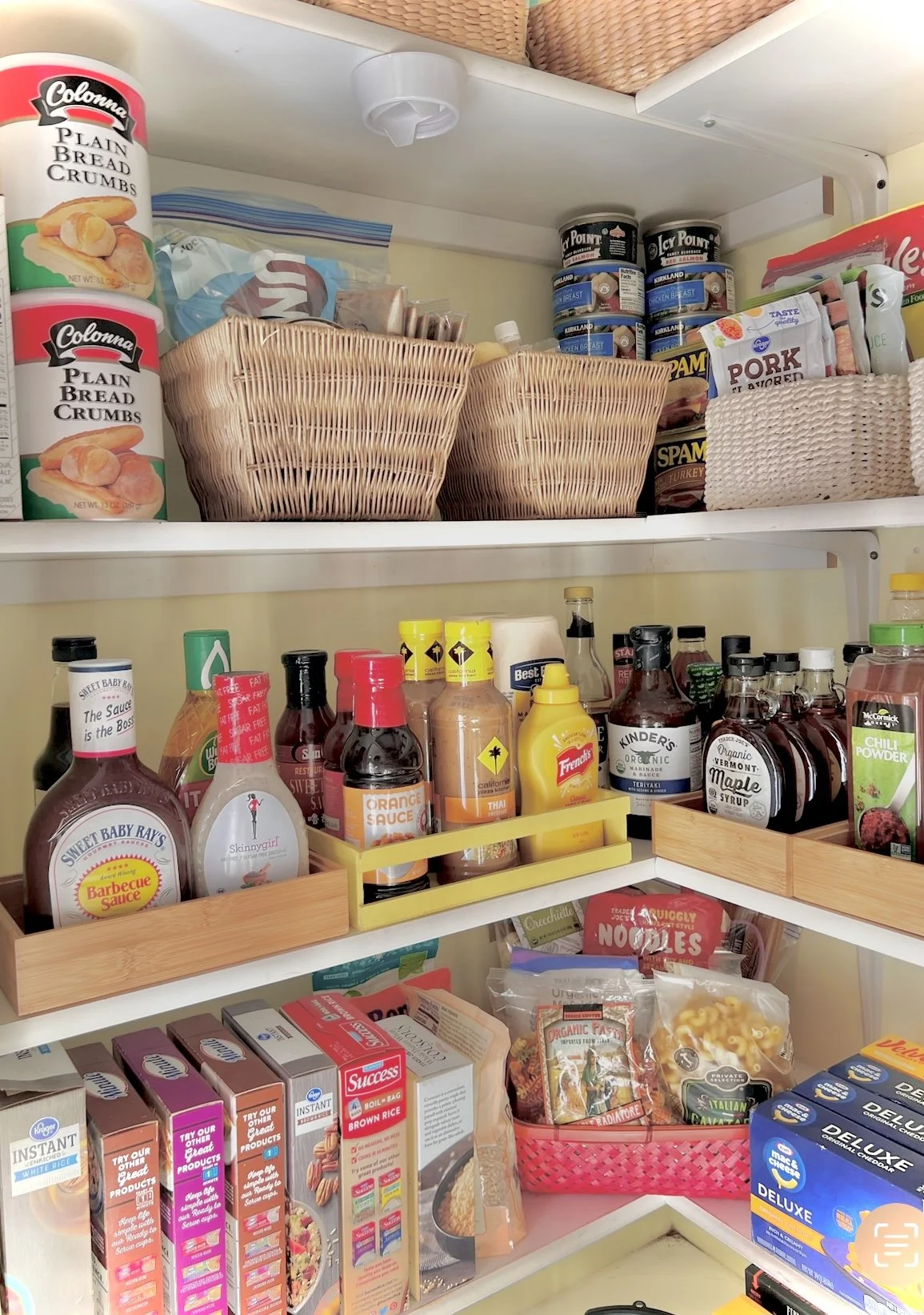 Inside a pantry with various canned goods, sauces, and pantry staples on shelves and in baskets.