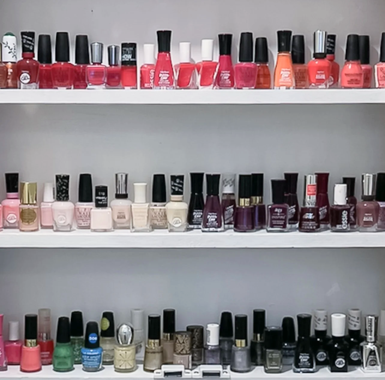 Organized nail polish collection grouped by color on shelves