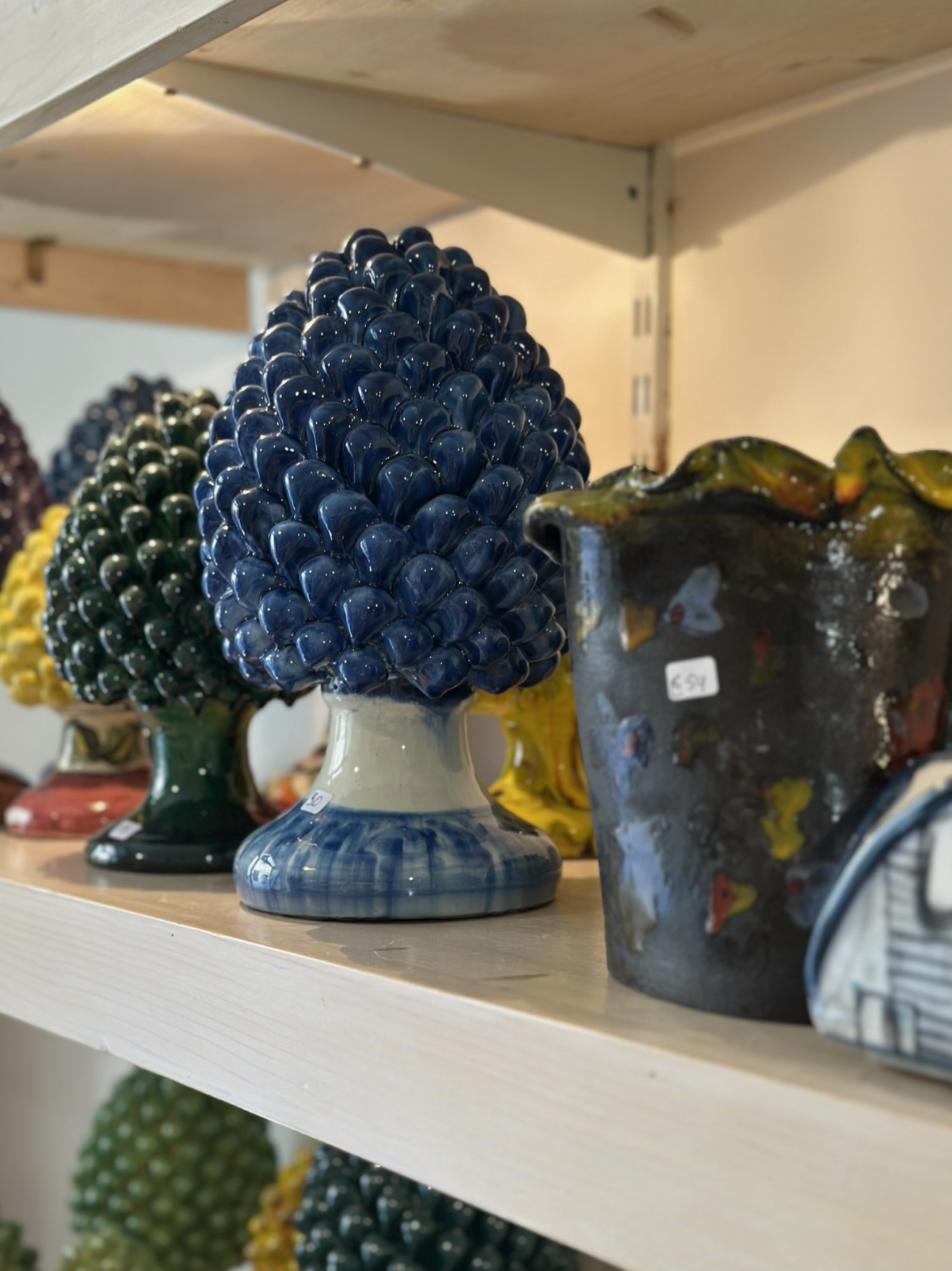 Colorful ceramic art sculptures arranged on a shelf, resembling pine cones or conical shapes, in shades of blue, green, and yellow.