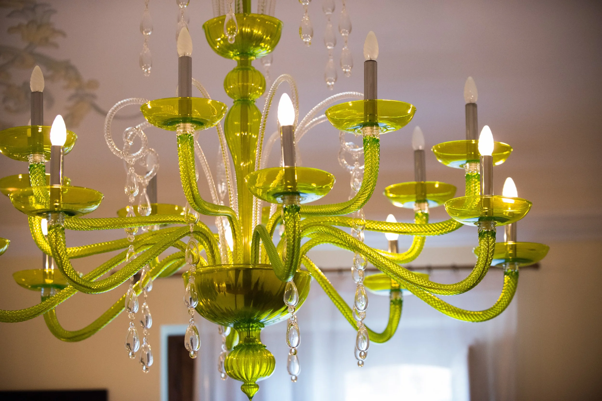 A bright yellow-green chandelier with multiple arms, topped with candle-shaped lights, hanging from the ceiling with crystal decorations.