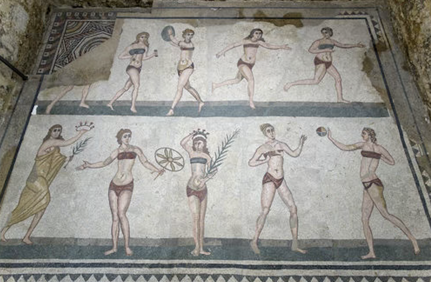 Cityscape with a domed church in the foreground and a volcano erupting in the background, partially framed by green leaves.