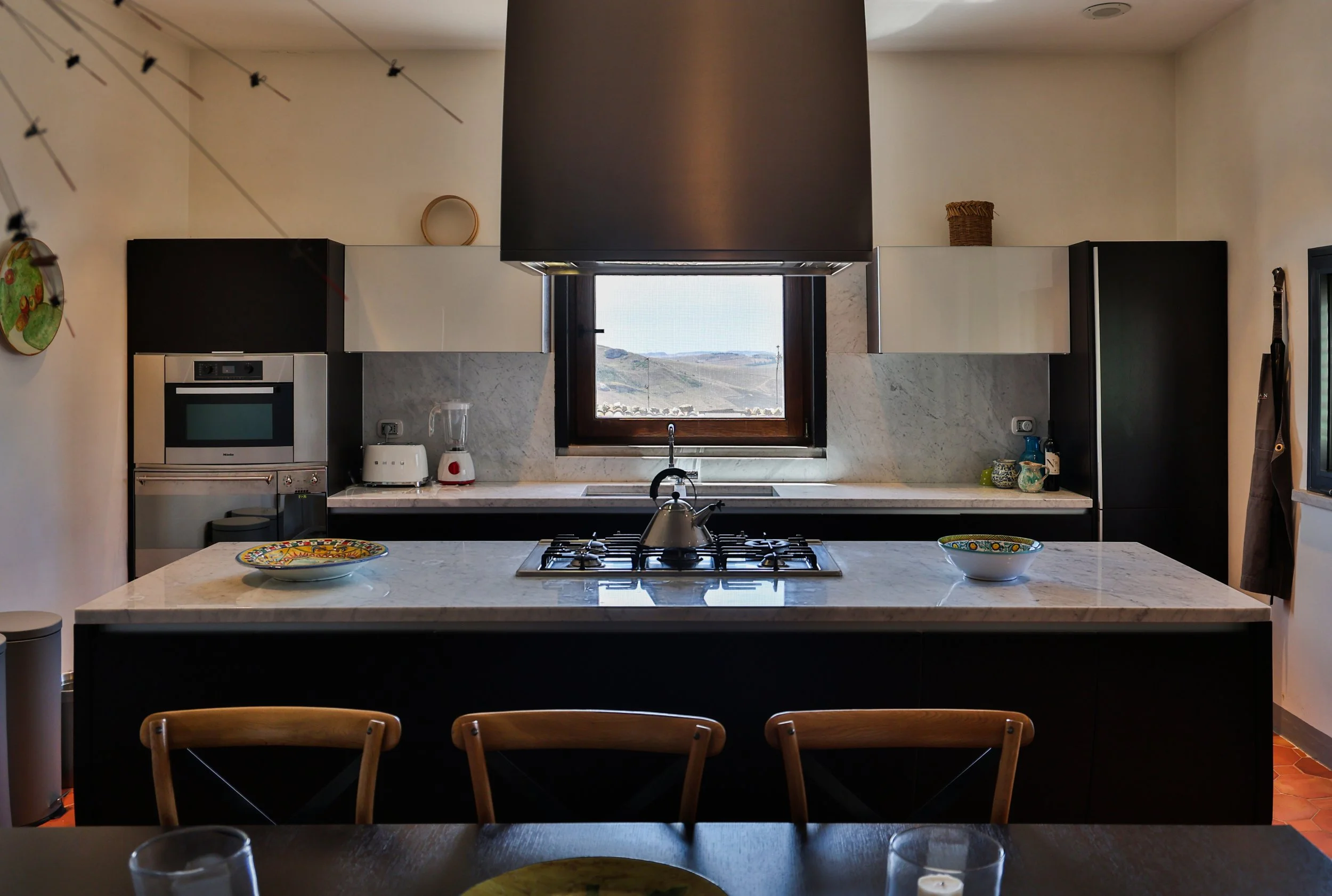 Modern kitchen with marble countertops, wooden chairs, black and white cabinets, a window, and various appliances.
