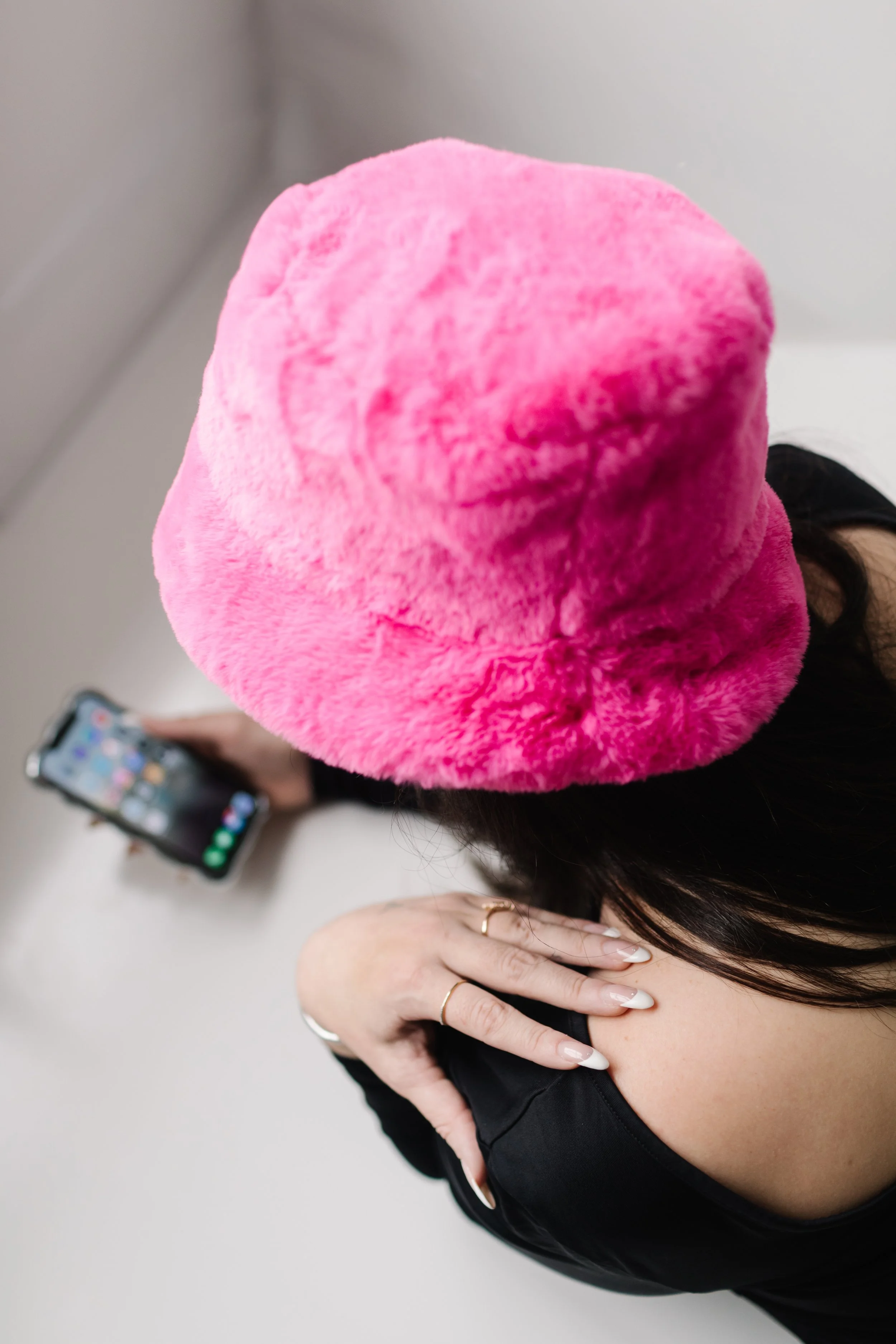 Top view of a woman wearing a pink fluffy hat, holding a smartphone in her right hand, and resting her left hand on her shoulder.