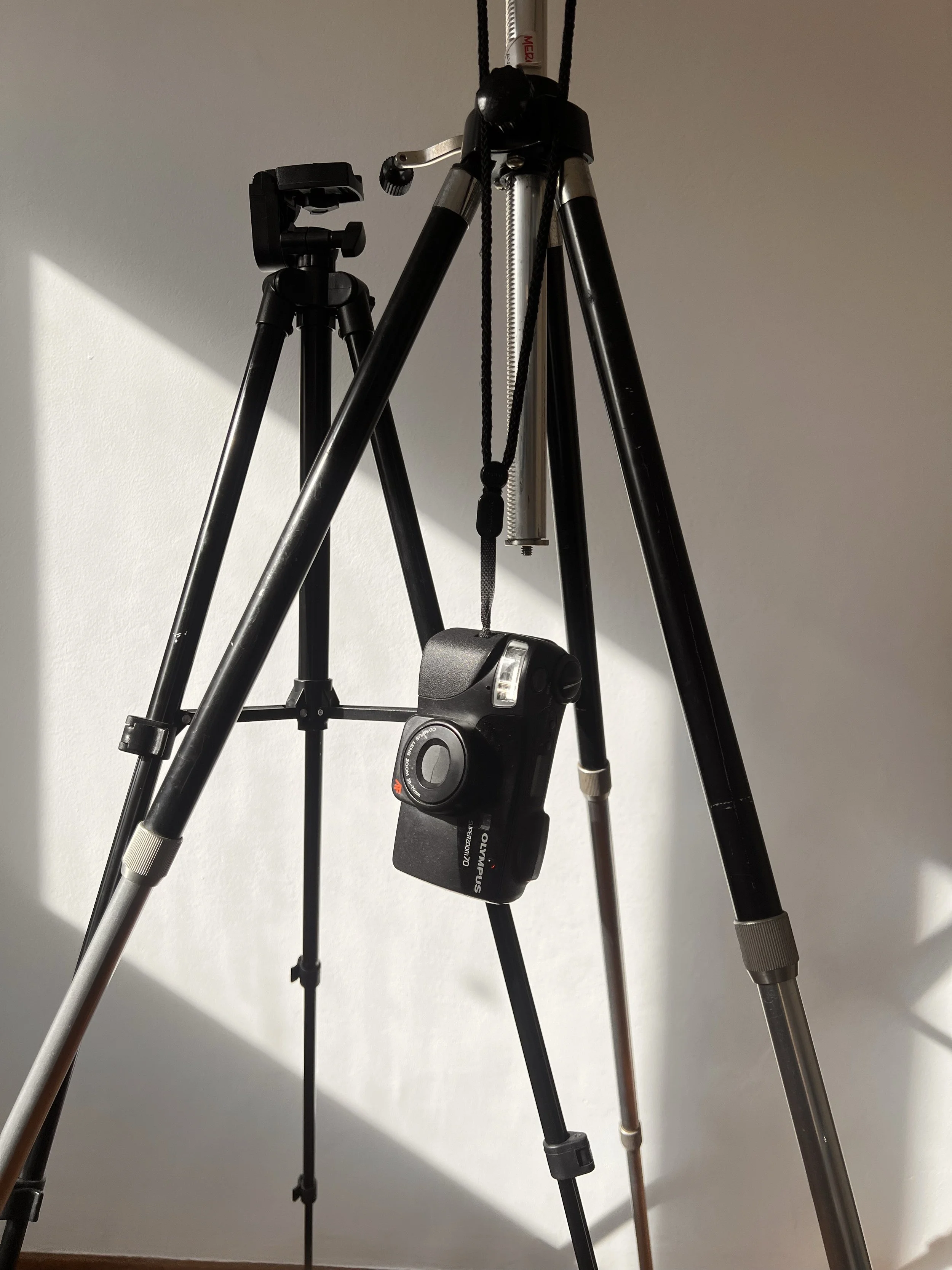 Two tripods and a camera on a plain wall
