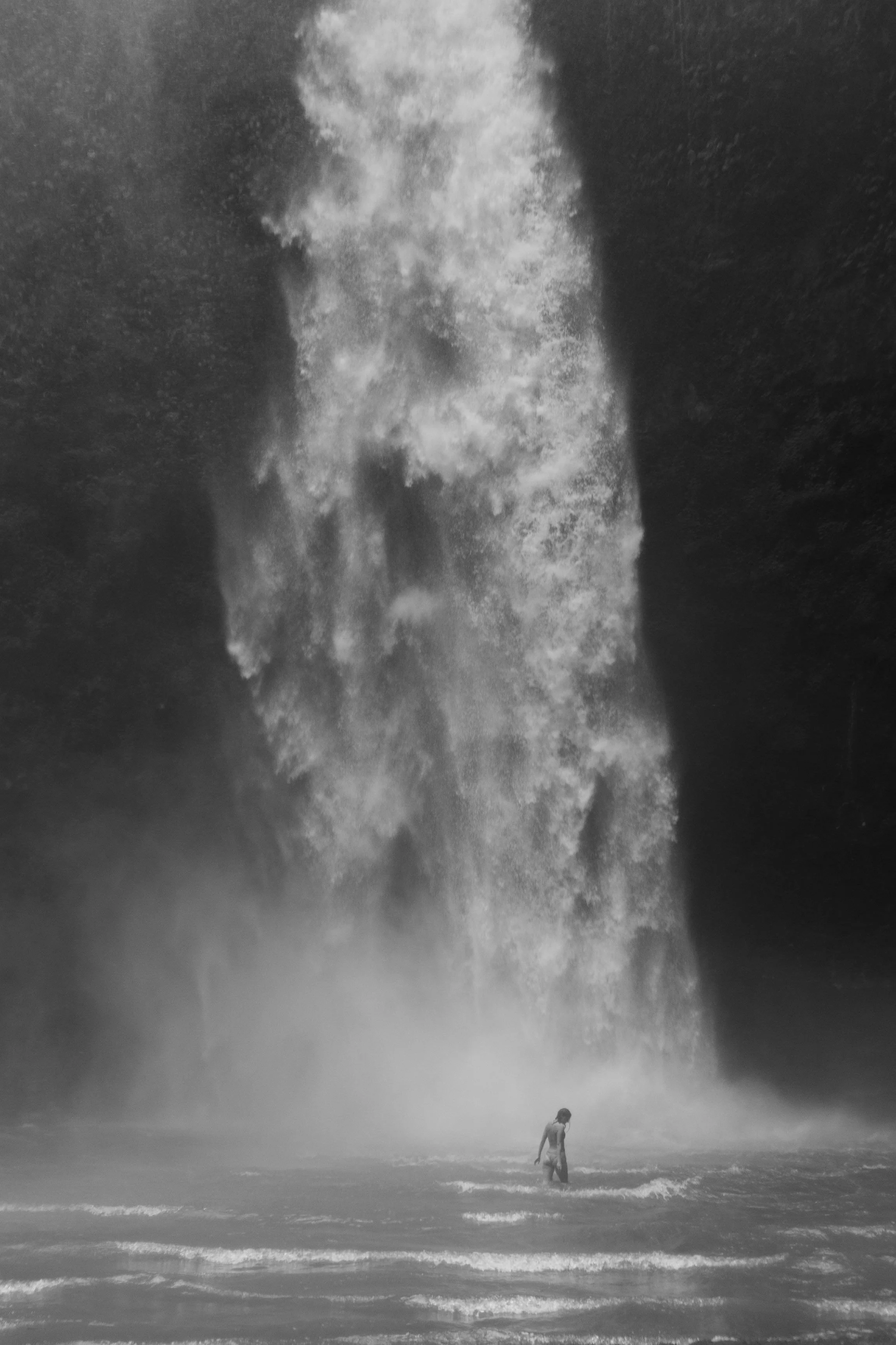A person standing in front of a large waterfall, with water splashing around.