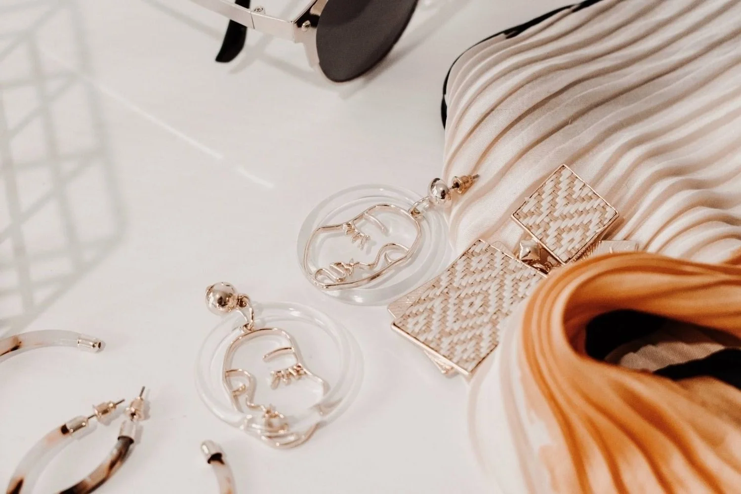Fashion accessories including gold earrings, a face-designed necklace, and woven pattern earrings, along with a striped fabric and orange hair.