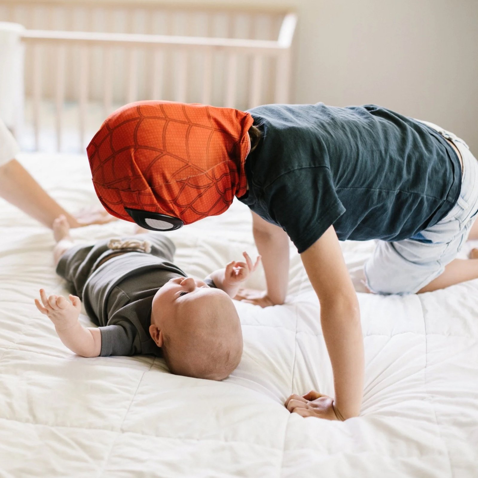 Two children on a bed, one dressed as Spider-Man leaning over the other child who is lying on the bed, looking up.