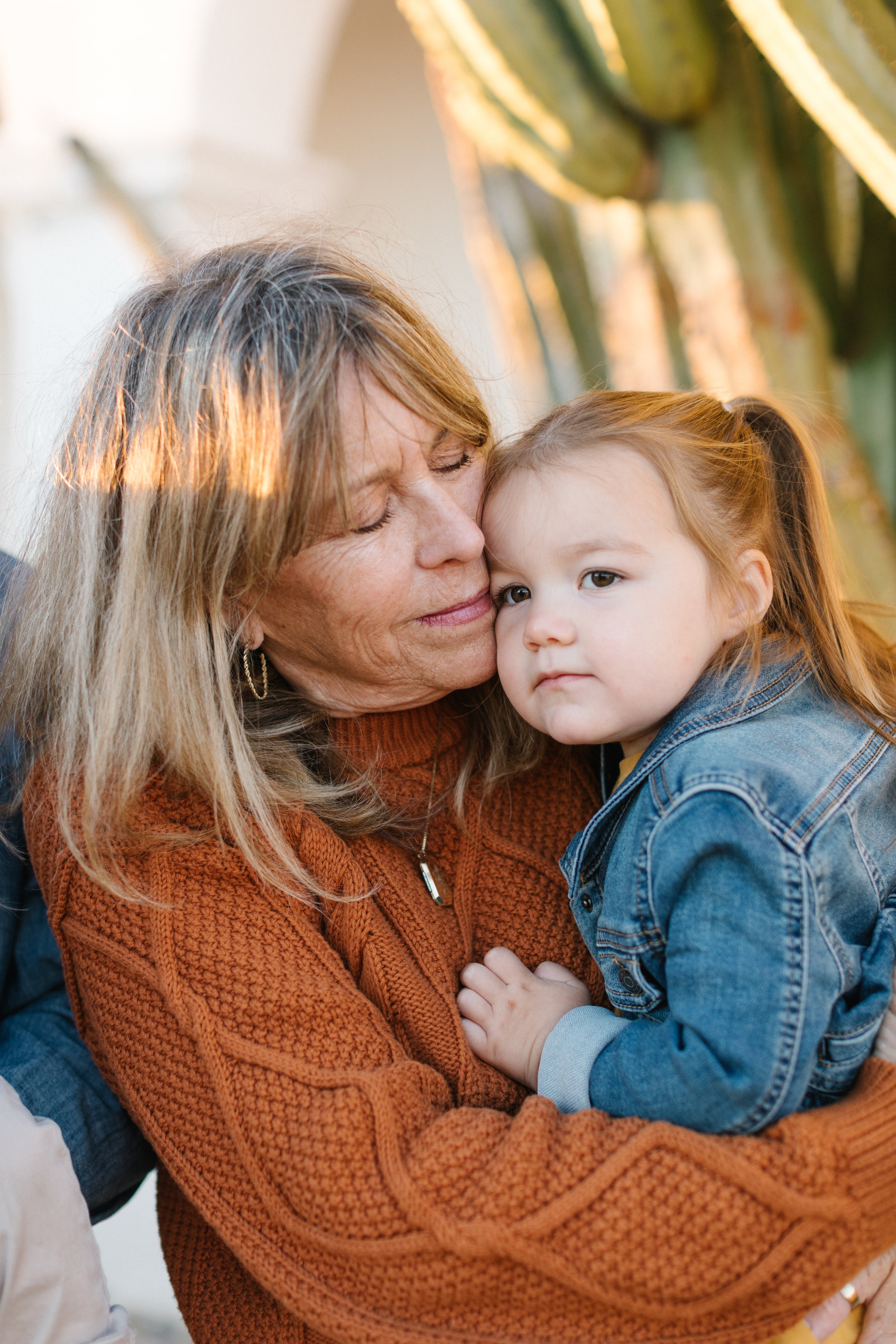 An older woman and a young girl hugging outdoors, with a cactus in the background.