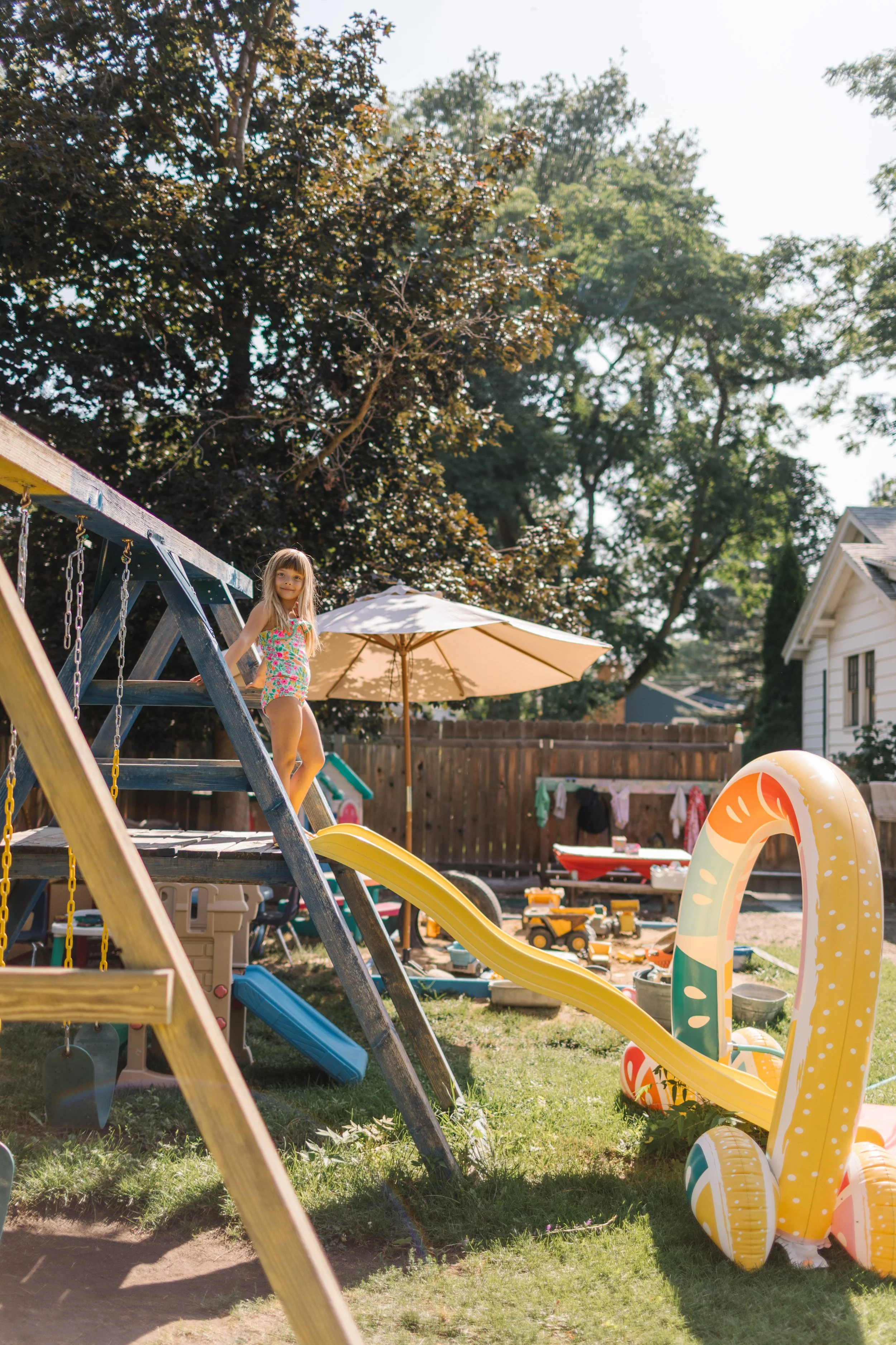 Child on a playset in a backyard with toys, umbrellas, and trees in in Boise, Idaho.