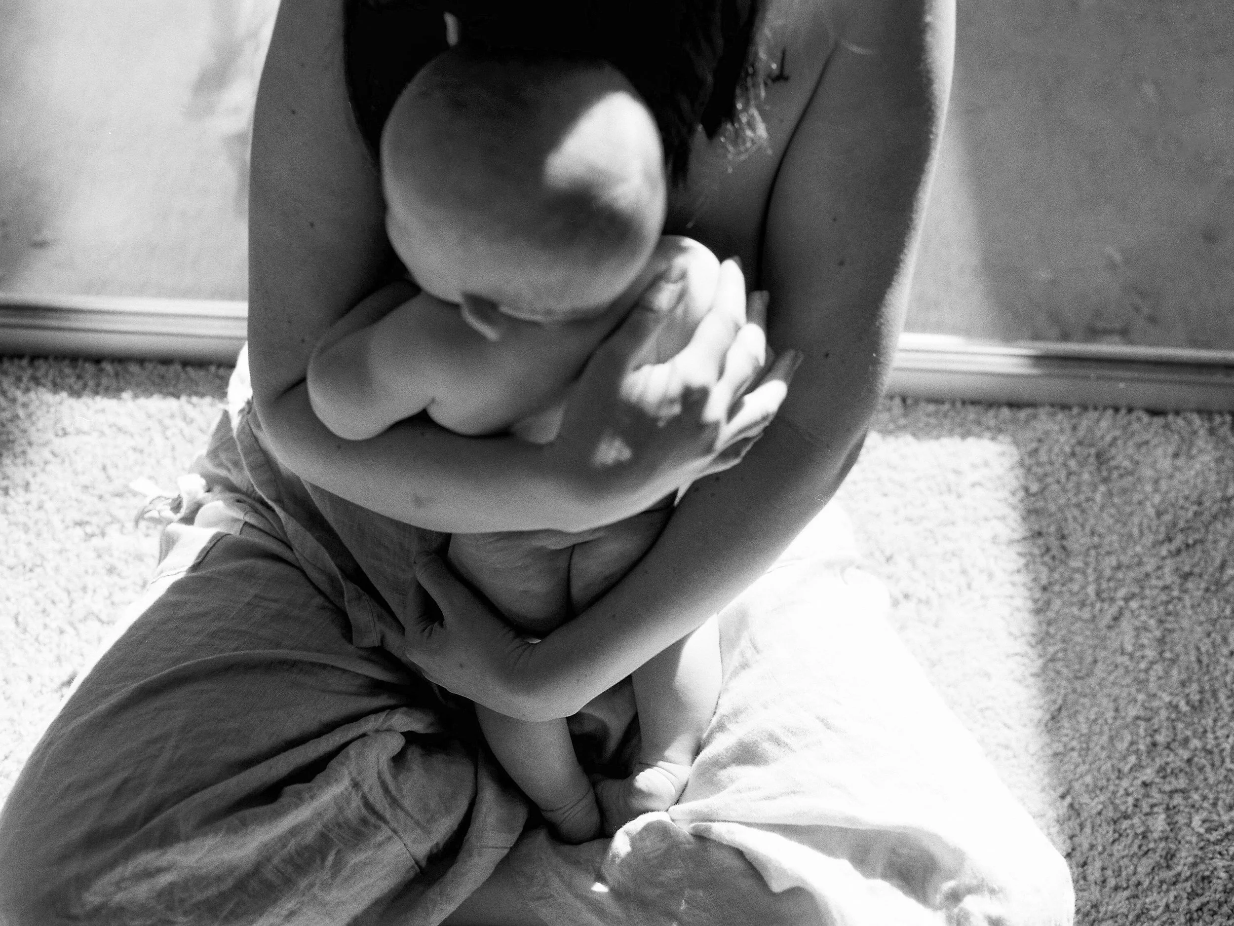 A person sitting on the floor, holding and comforting a crying child, who is hugging their knees.