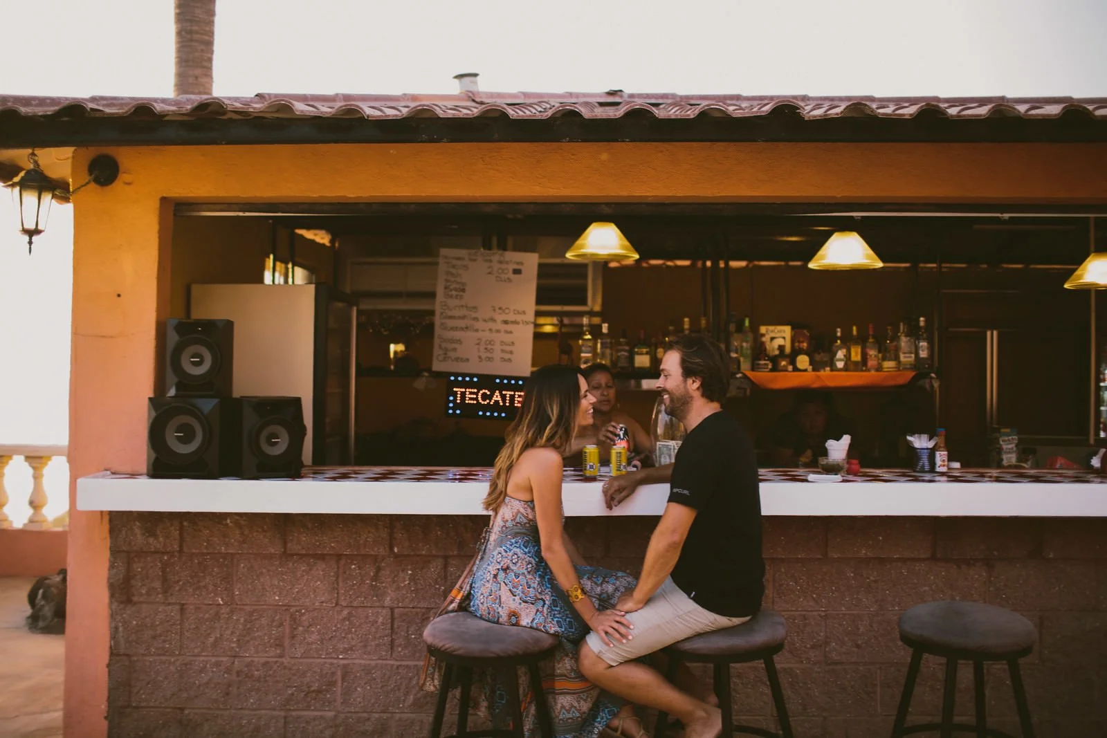 Couple laugh at a beachside bar at their engagement session in Mexico- - Destination Fine Art Wedding Photographer
