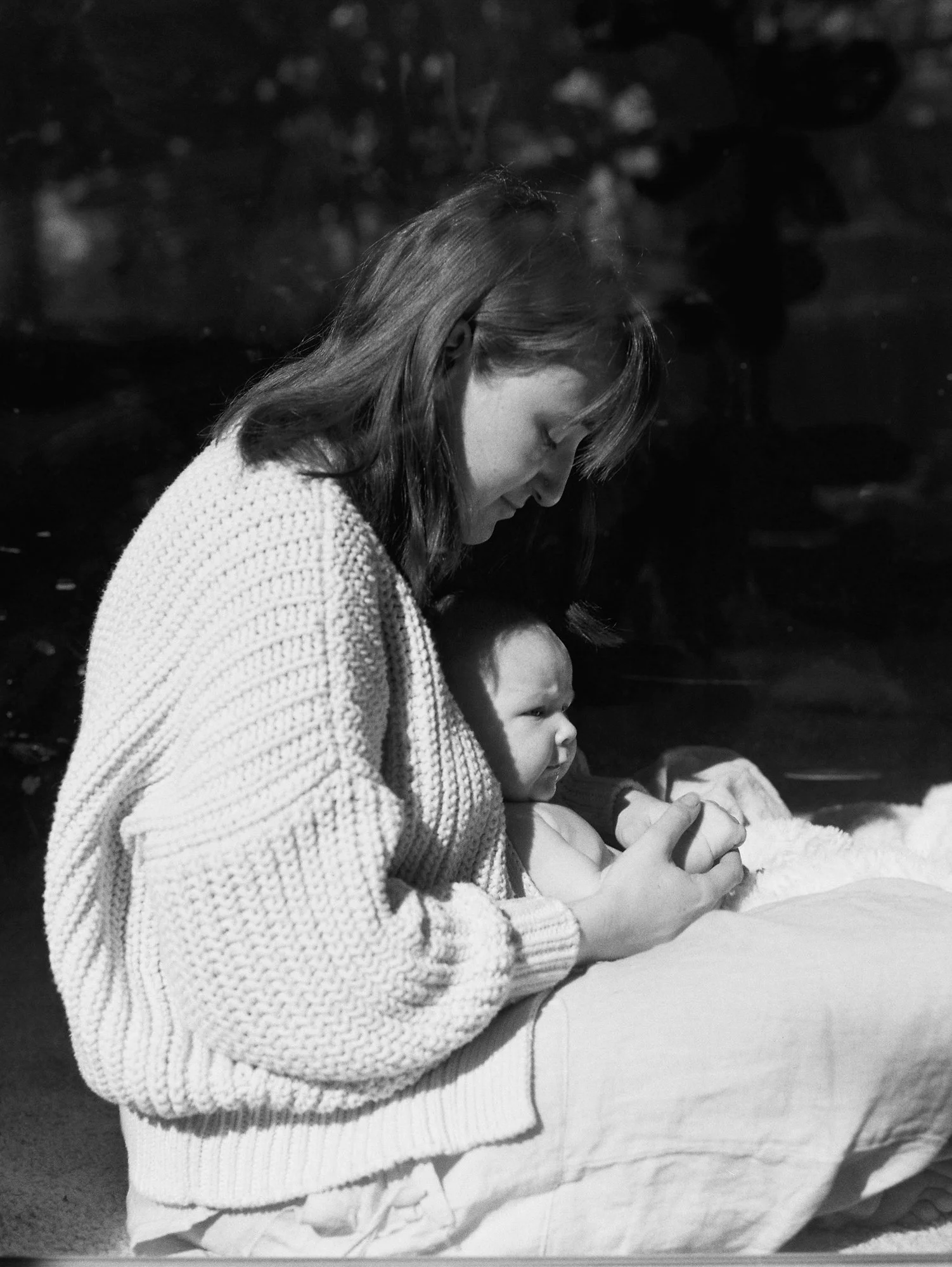 A woman and a small child sitting together outdoors in black and white, with the woman looking down and the child sitting on her lap.