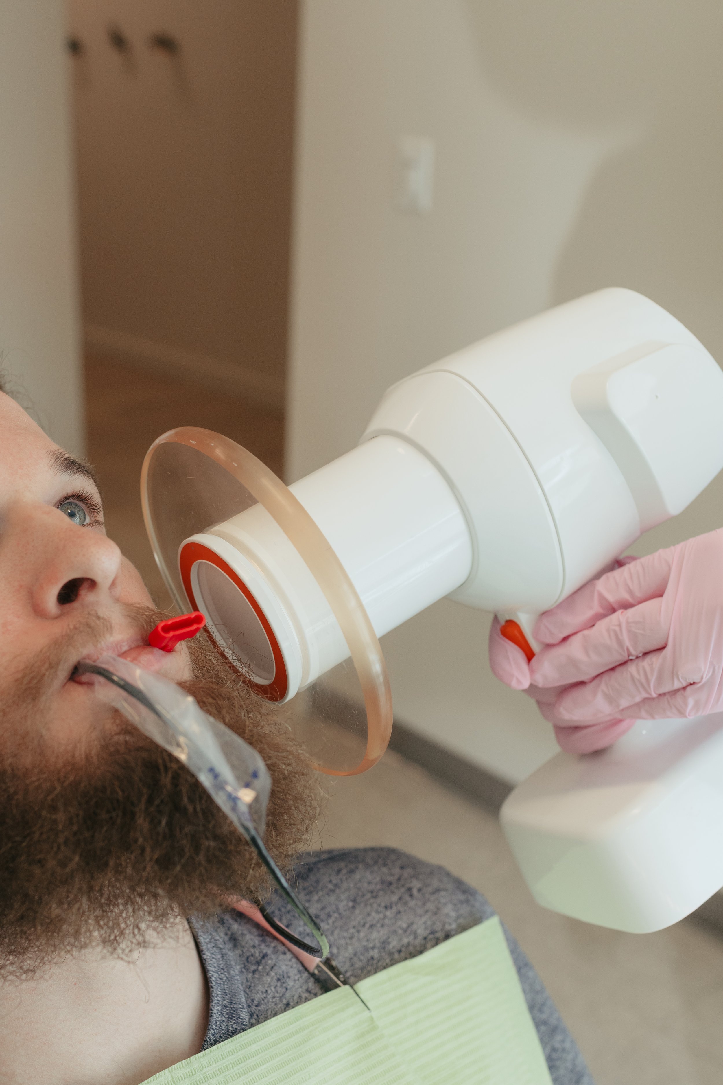 Person in a medical setting undergoing a breathing test with spirometry equipment, including a mouthpiece and a tube, held by a healthcare professional wearing pink gloves.
