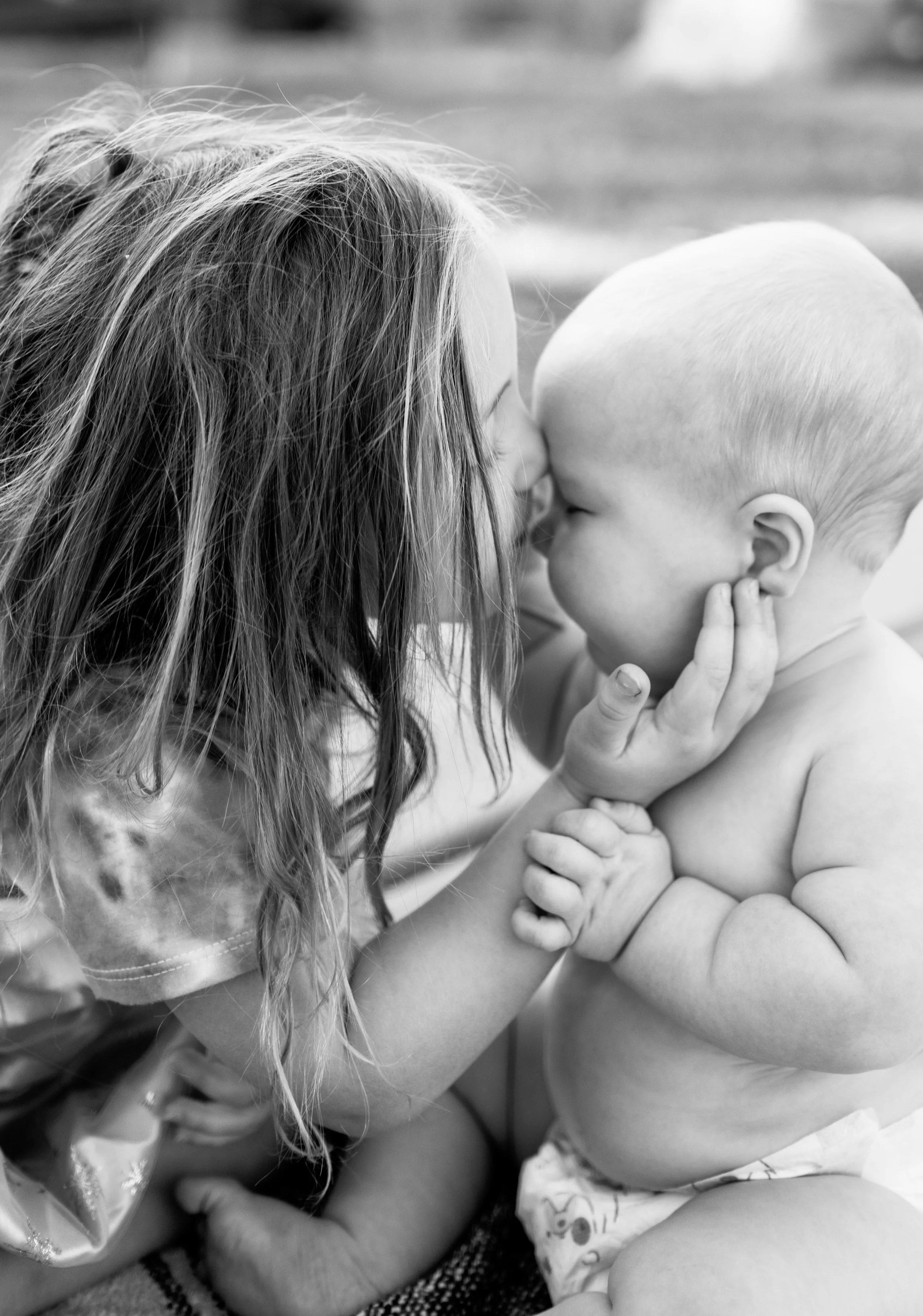 A young girl and a baby boy touching foreheads and touching faces affectionately in black and white.