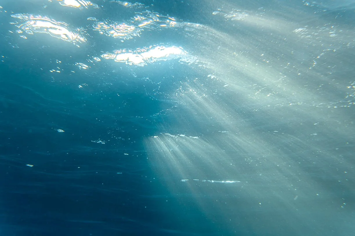 Underwater view of the ocean with sunlight rays penetrating the water surface.