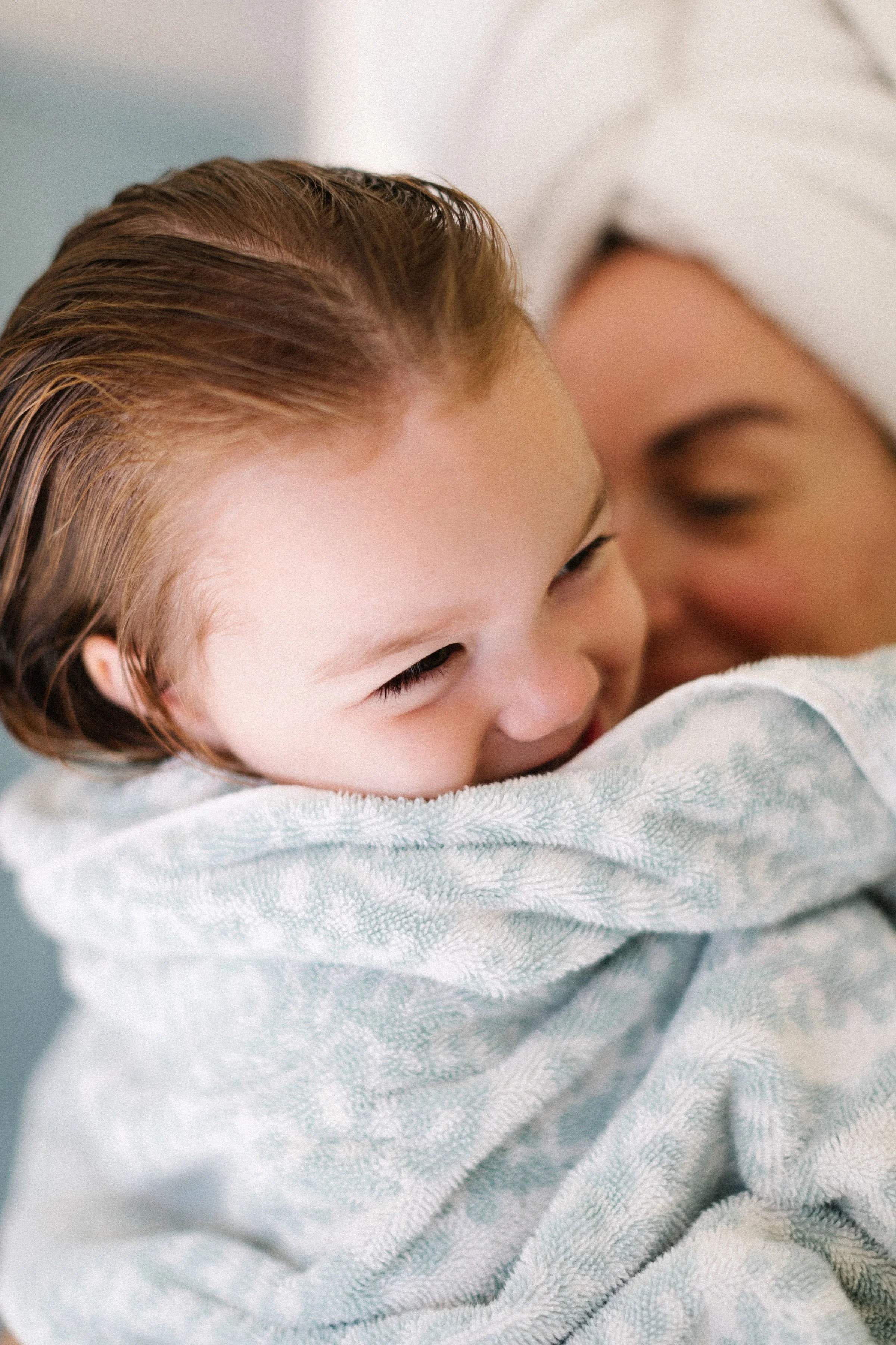 A young boy with wet, slicked-back hair is smiling while being hugged by a person in a hospital gown, in a warm and caring moment.