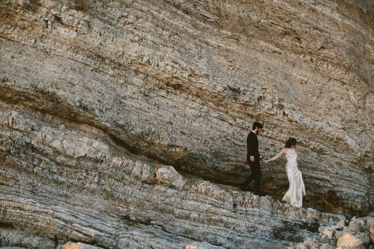 Couple walk down a cliffside together on their wedding day