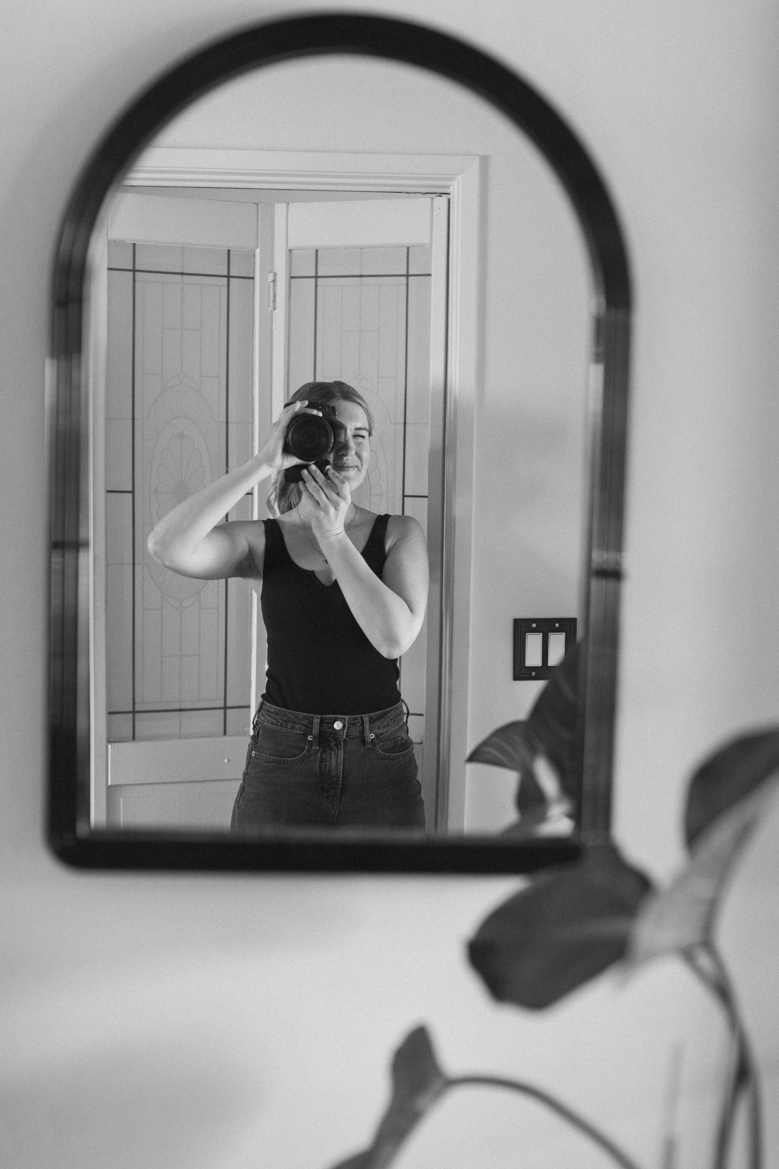 A woman taking a selfie using a camera in a mirror, smiling, with a flower in the foreground.