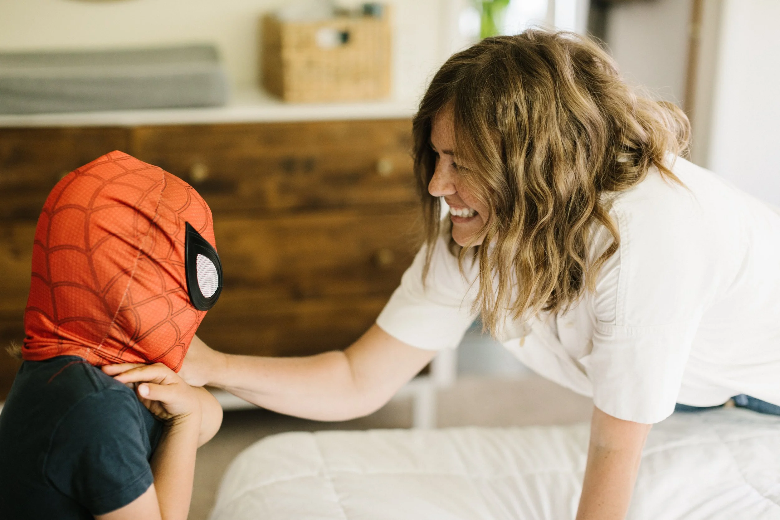 A woman smiling and reaching out to a child wearing a Spider-Man hoodie.