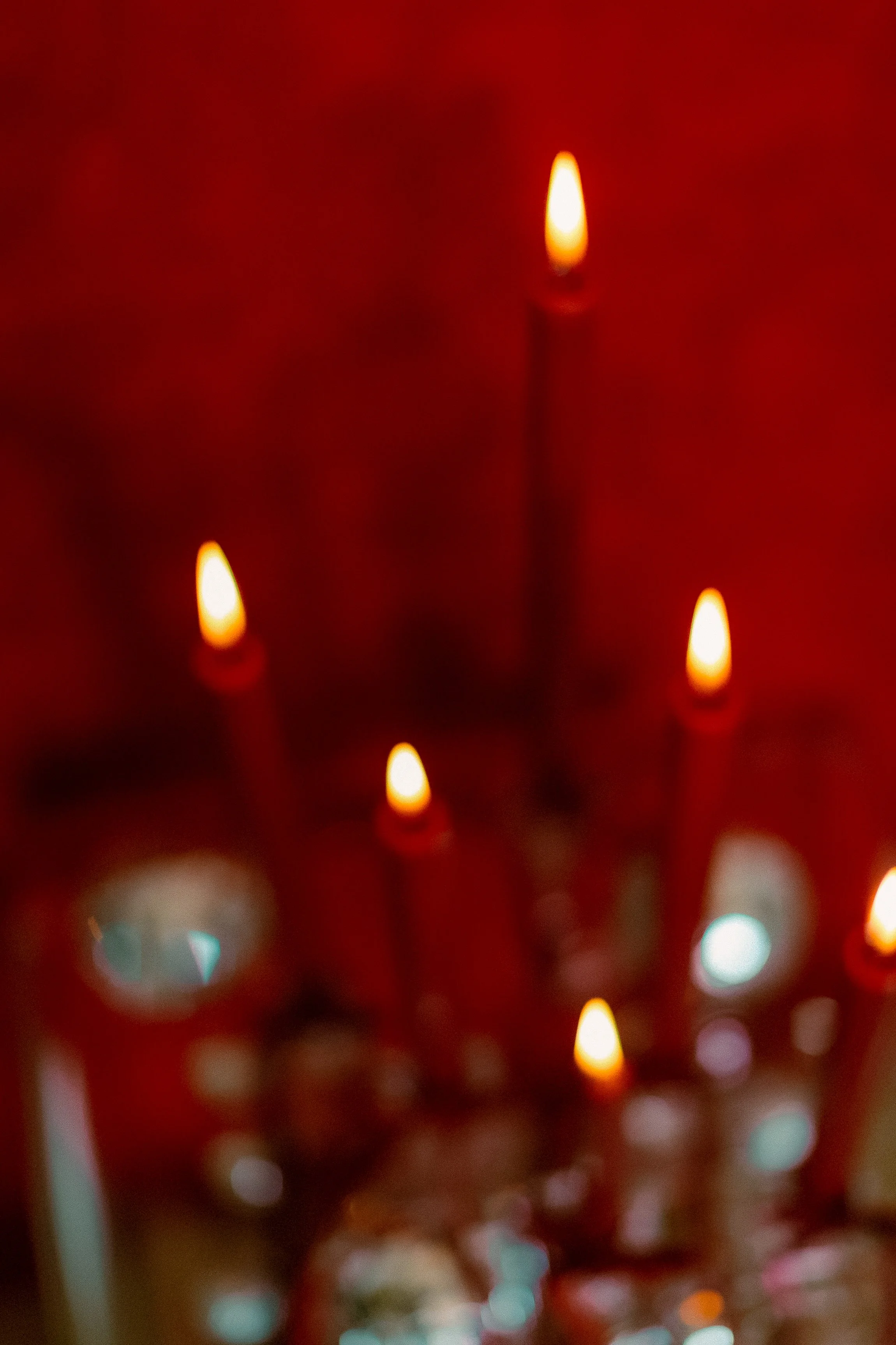 Close-up of several lit candles against a red background, with soft glowing flames.