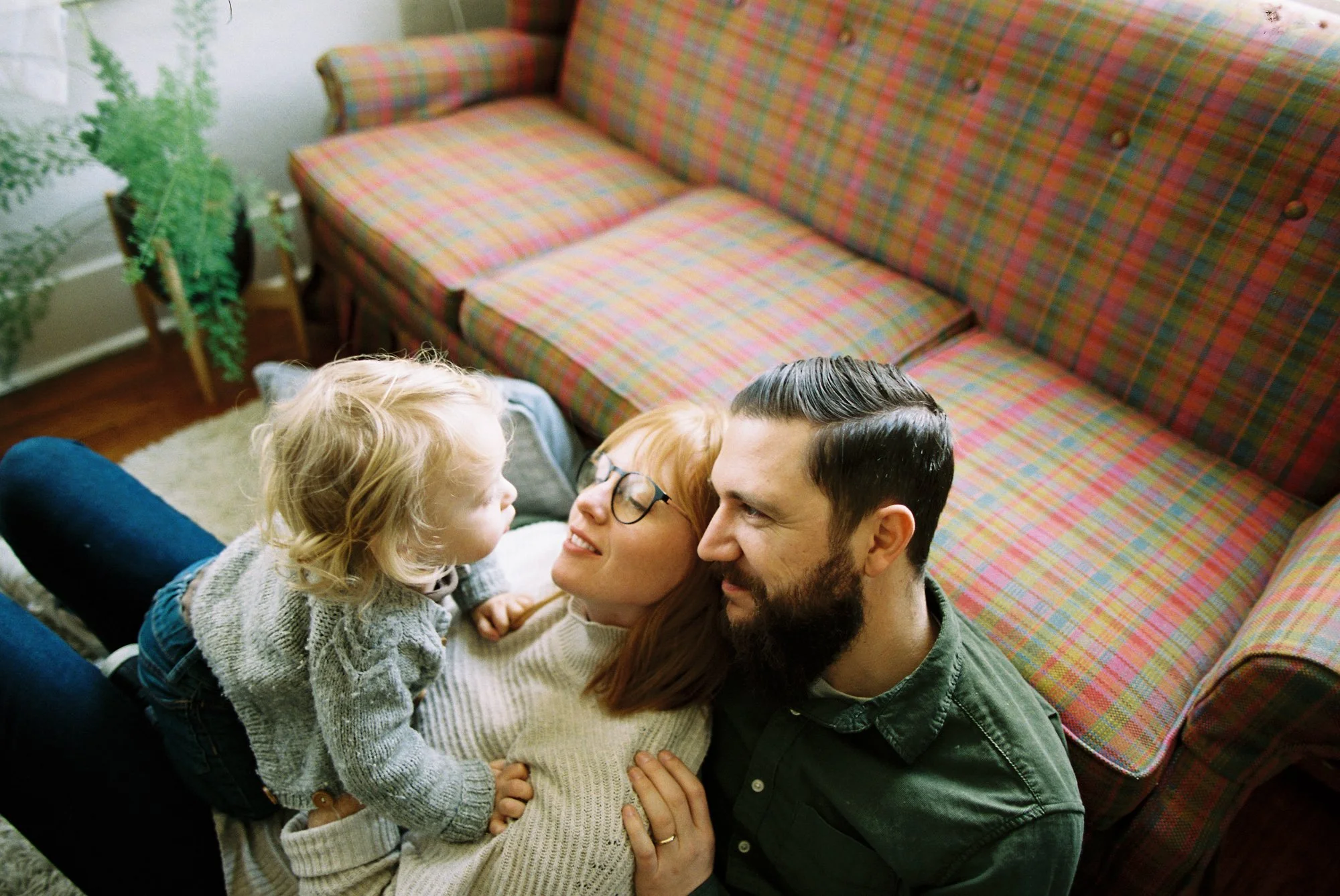 A family of three, consisting of a mother, father, and young daughter, lying on the floor together in a living room.