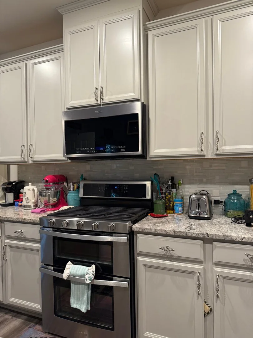 Kitchen with white cabinets, stainless steel stove, microwave above, and various small appliances and utensils on the countertop.