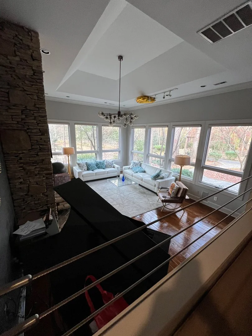 Living room with large windows, two white sofas with blue cushions, a glass coffee table, a rocking chair, multiple standing lamps, and a stone accent wall.