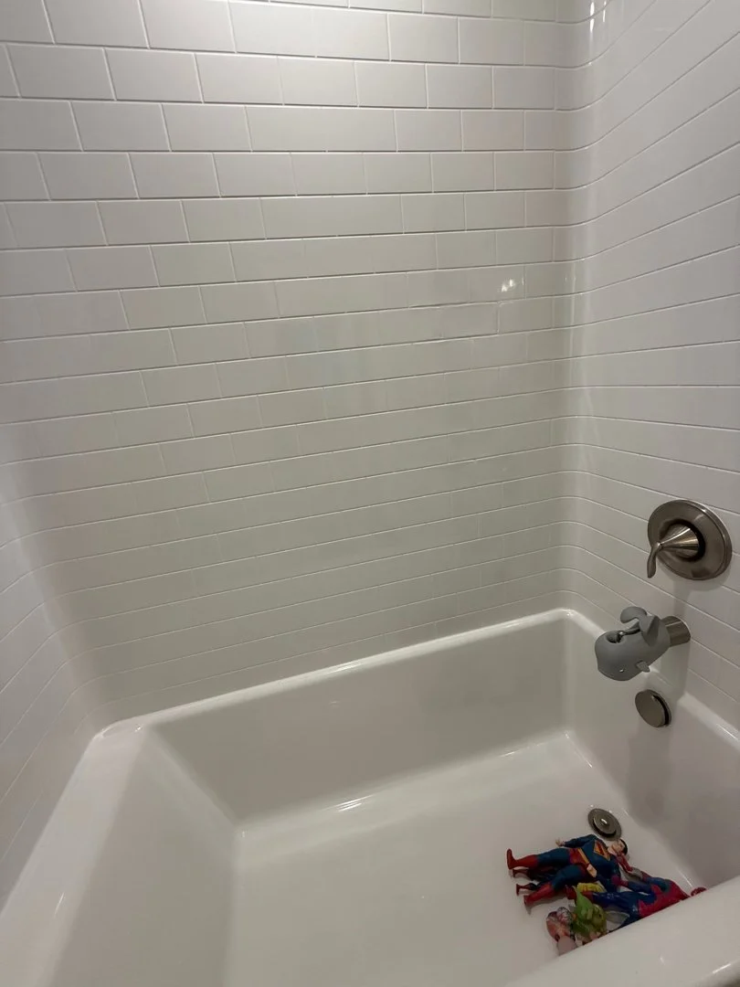 Empty bathtub with white tiled walls, a bath spout, a lever handle, and a drain with a pile of toys inside.