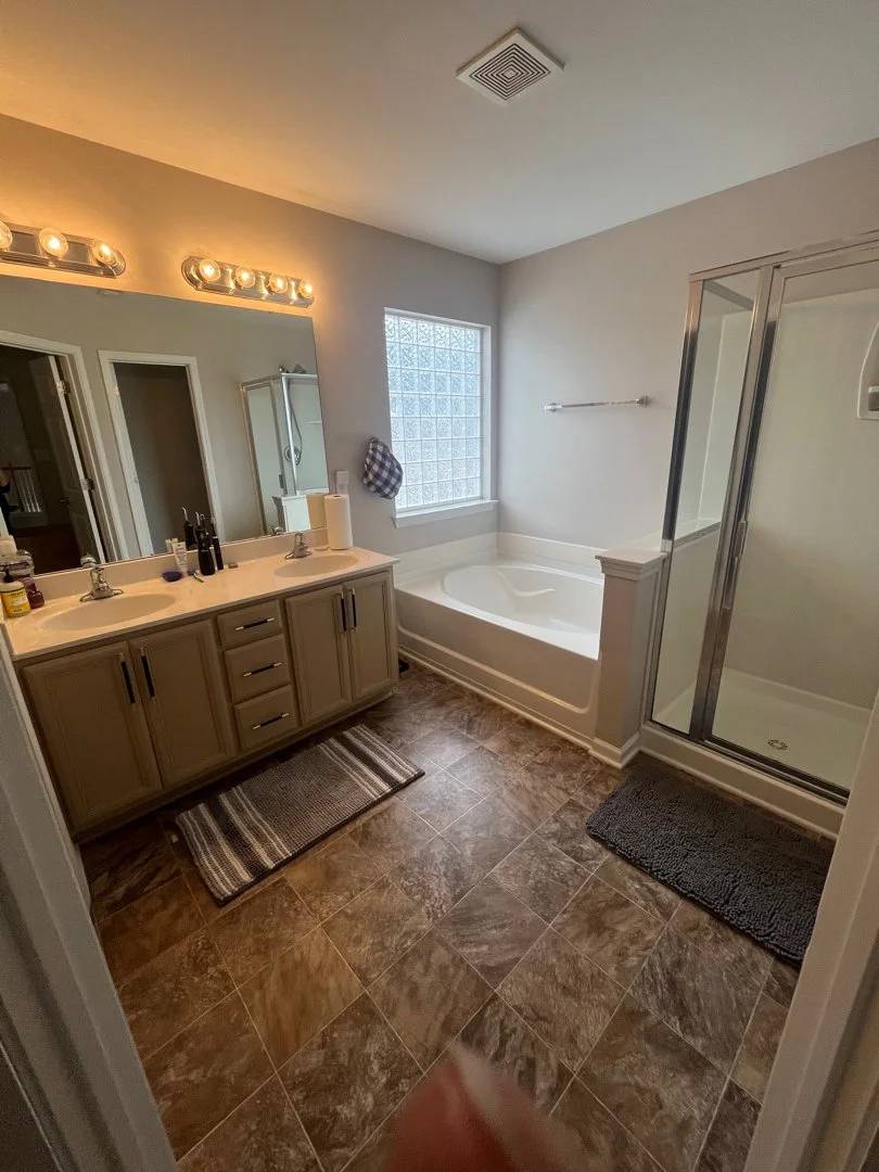 Bathroom with dual sinks, large mirror, bathtub, walk-in shower, window with glass blocks, and tiled flooring.