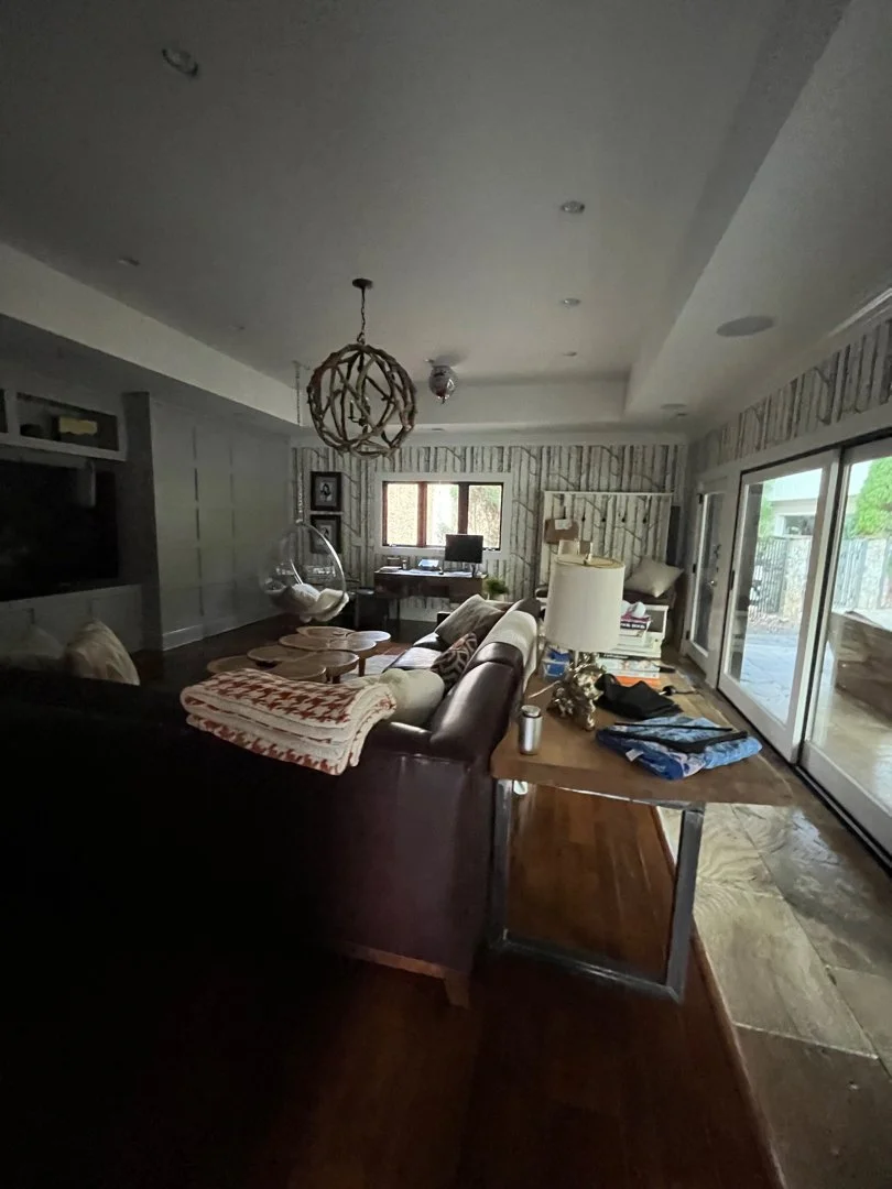 Living room with a sofa, coffee table, and a hanging chair near the window, with a desk, computer, and sliding glass doors leading outside.