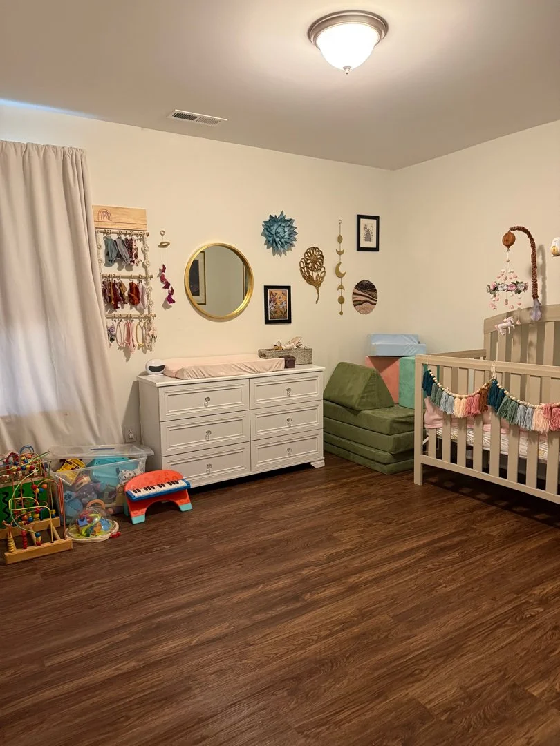 A children's nursery with a crib, green cushioned chair, dresser, and various toys on the floor.