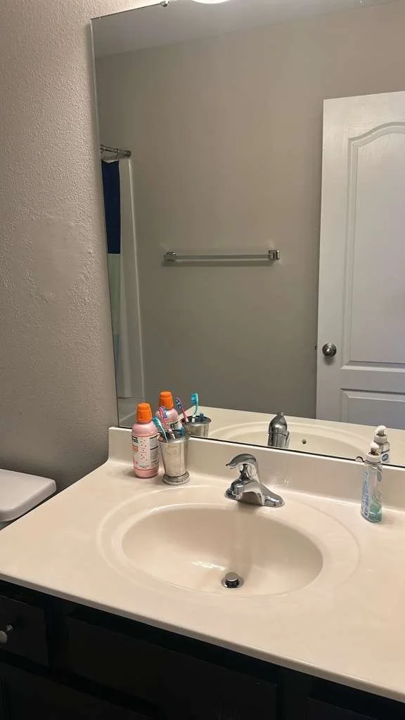 Bathroom sink countertop with a mirror, toothbrush holder with toothbrushes, soap dispenser, and bottles of medicine or lotion.