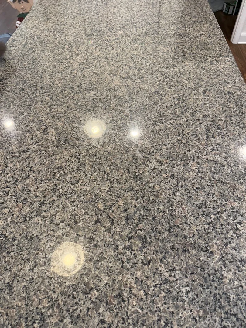 A close-up view of a speckled granite countertop with reflections of ceiling lights.