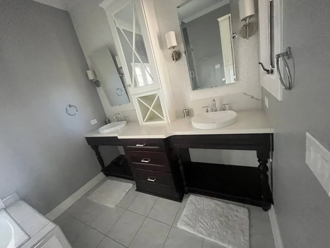 Bathroom vanity with two sinks, mirrors, wall-mounted lights, and a cabinet in a modern style.
