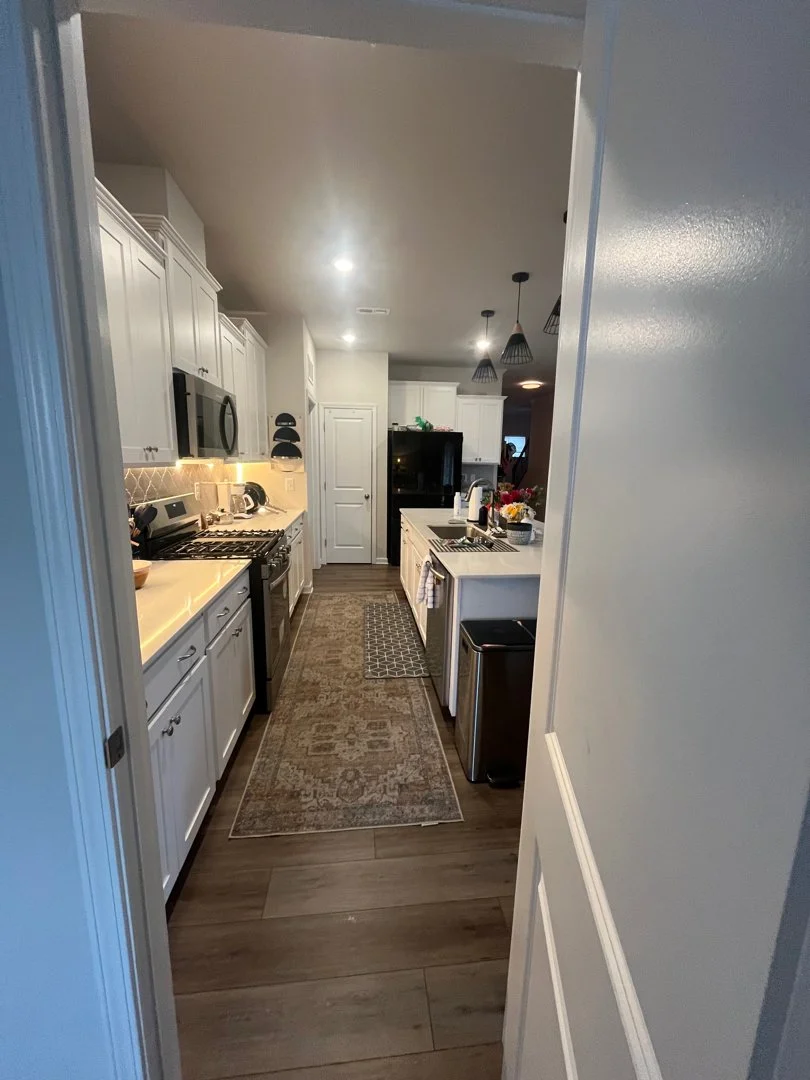 View of a modern kitchen with white cabinets, stainless steel appliances, a kitchen island with a flower arrangement, and decorative pendant lights hanging from the ceiling.