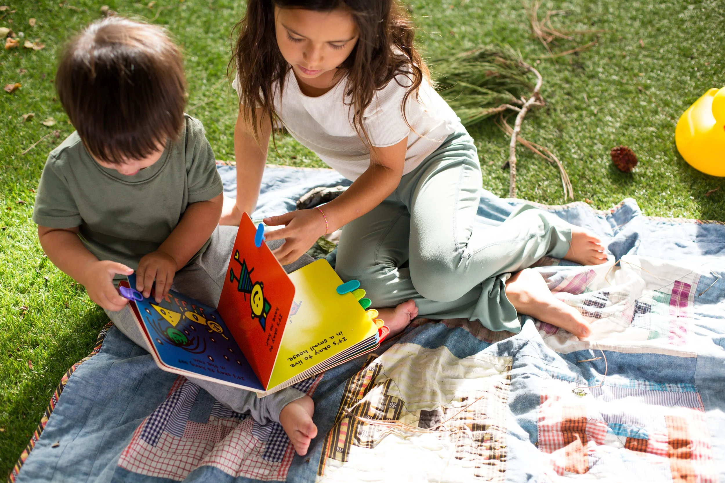 Two childen sitting outside reading a book together, using Flipps page turning tools to read board book.