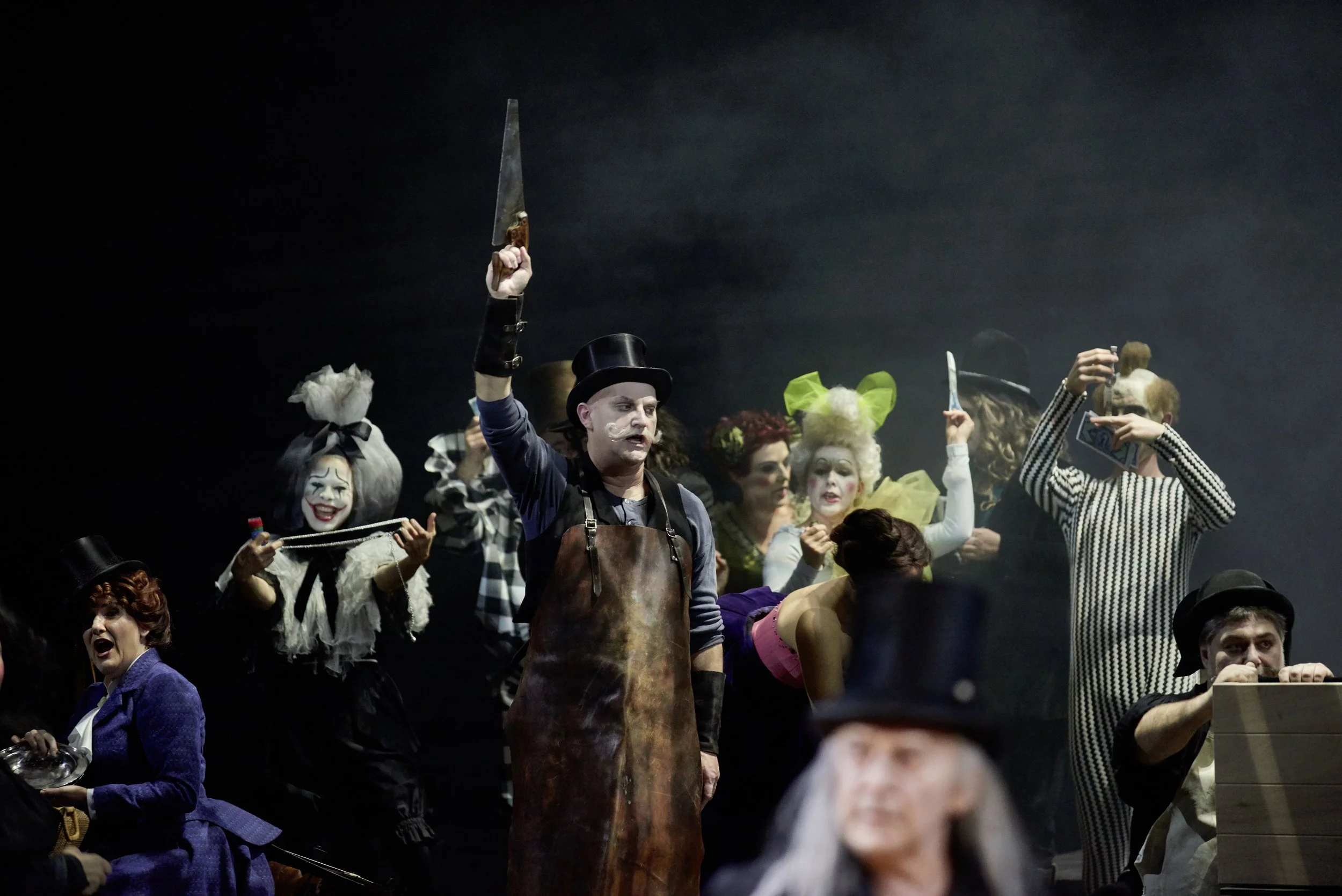 Bühnenaufnahme eines Theaters mit mehreren Schauspielern in viktorianischer oder clownartiger Kleidung, einige mit Gesichtern bemalt, in dramatischer Pose, wohl für eine Theaterproduktion oder Varieté.