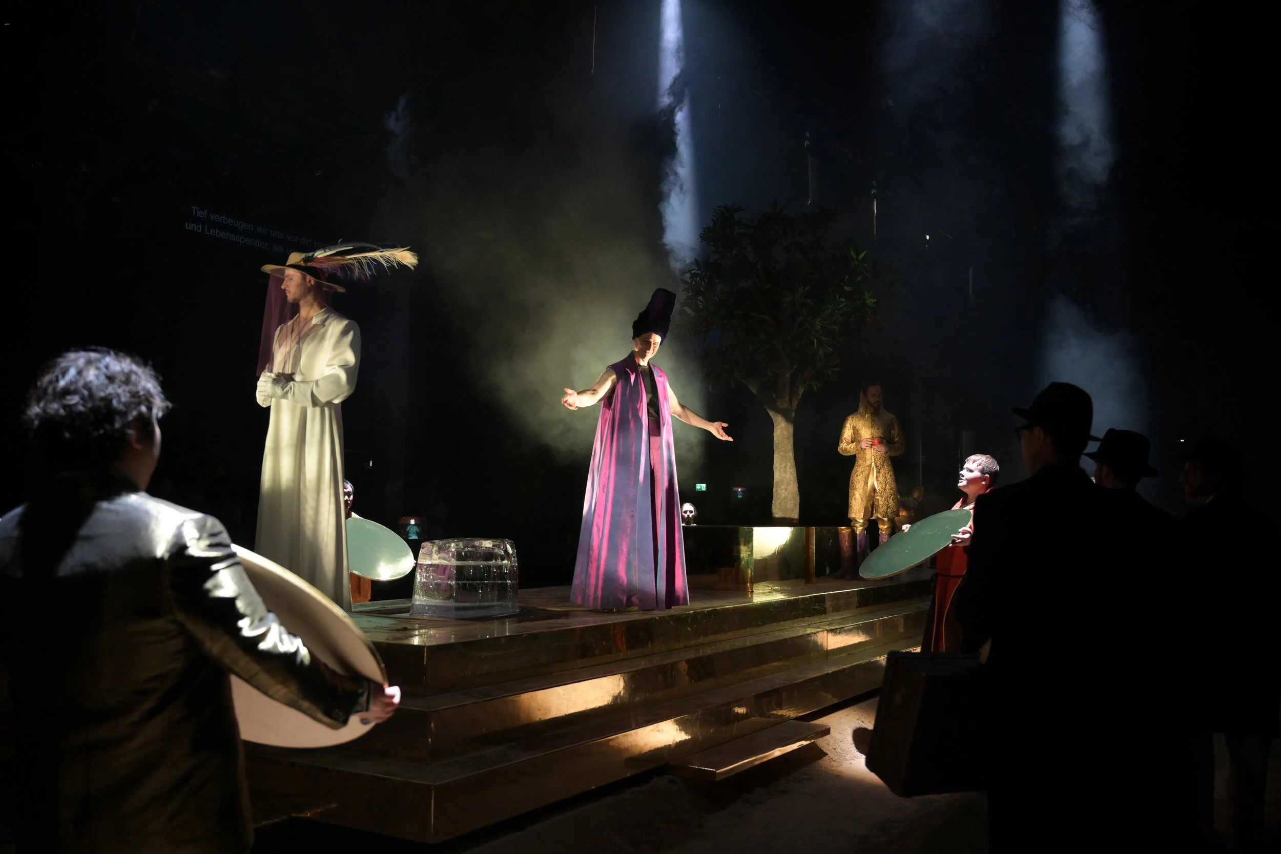 Bühnenperformance mit Schauspielern in historischen Kostümen, dunkler Kulisse, Scheinwerfern, Publikum im Vordergrund