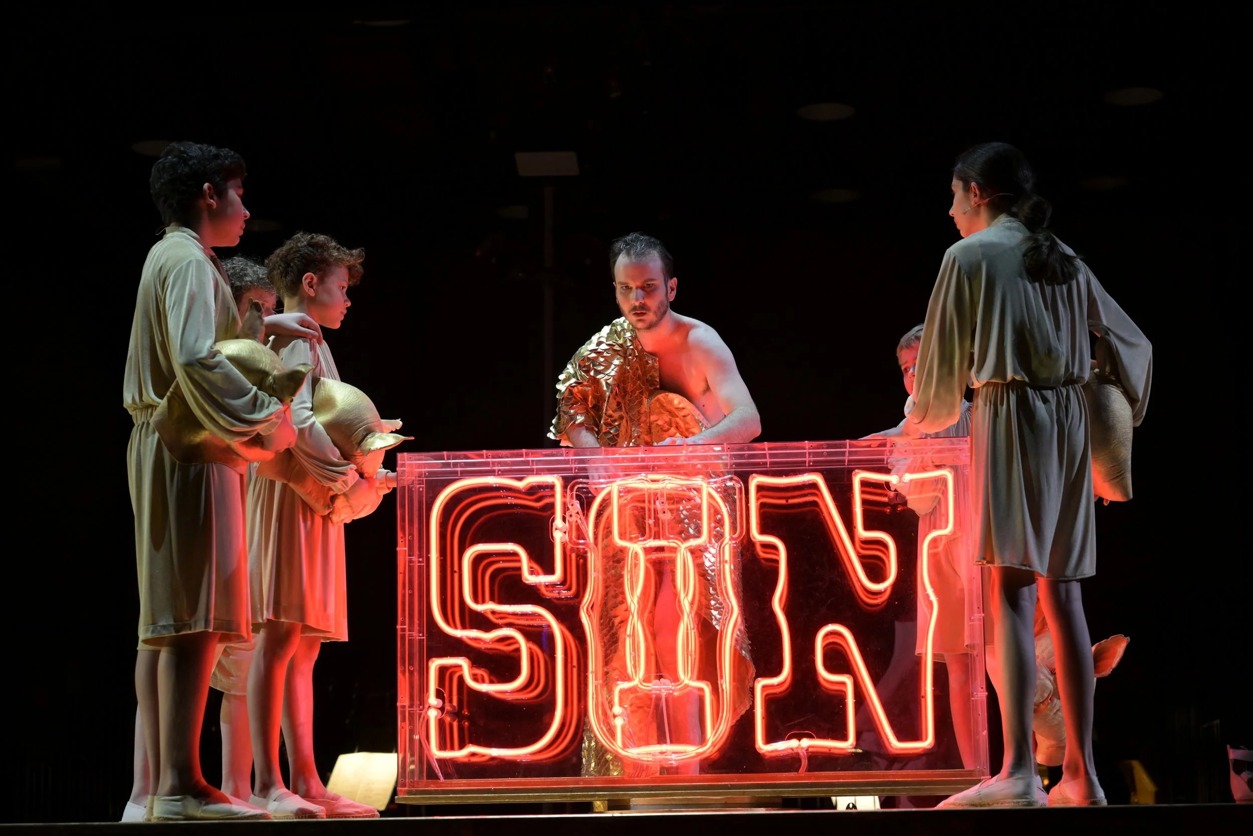 Schauspieler auf einer Bühne mit einem Neon-Schild, das 'SIGH' zeigt, in einer Szene einer Theaterproduktion.