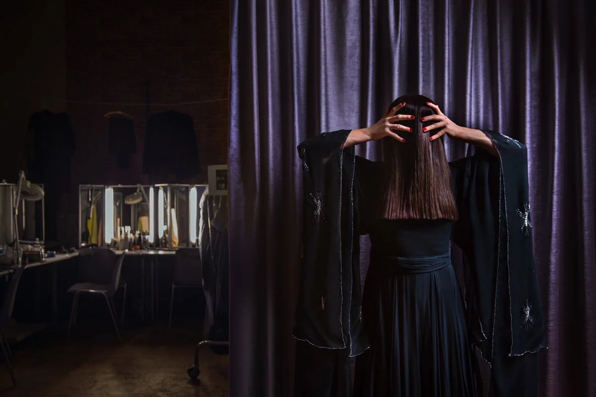 Frau steht vor einem Vorhang, Hände im Haar, im Theater- oder Kostümbereich